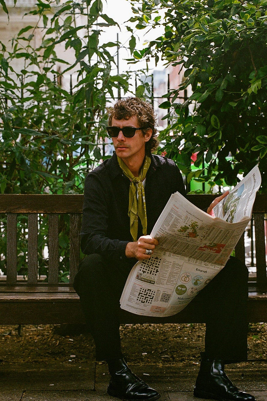 Man reading a newspaper on a bench in an urban setting