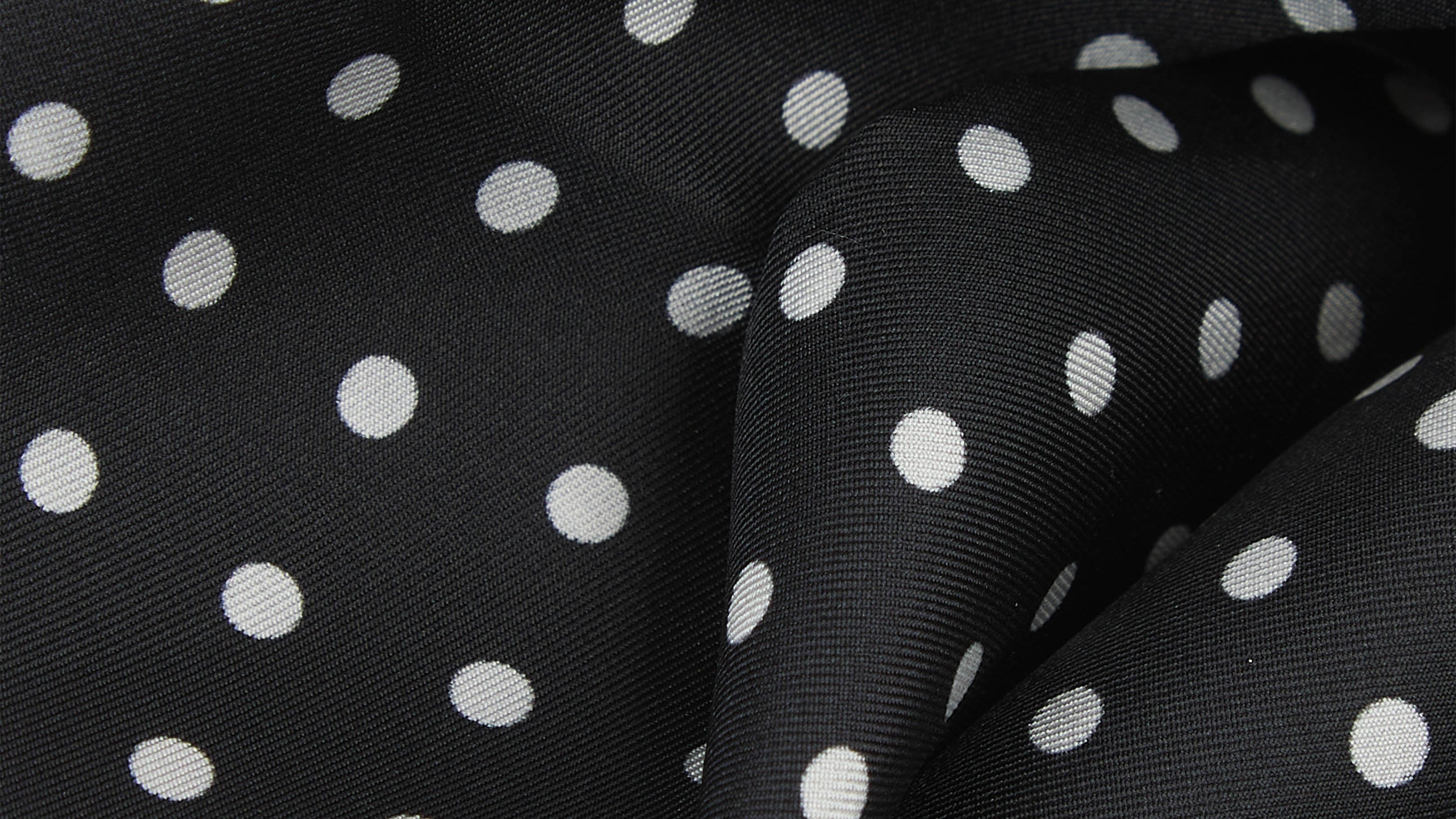 Black fabric with a white polka dot pattern, shown in a close-up draped view.