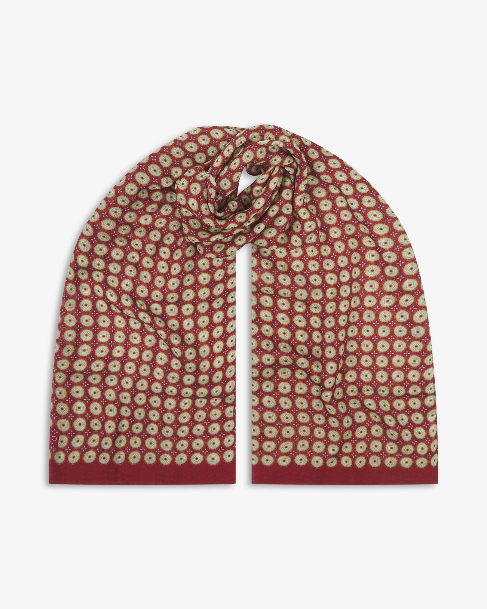 The Bellingham 'Gardenia' bohemian wide scarf looped with both ends parallel, showcasing intricate concentric circular motifs in green, gold, orange and blue on a rich maroon background across the soft modal and wool blend fabric.