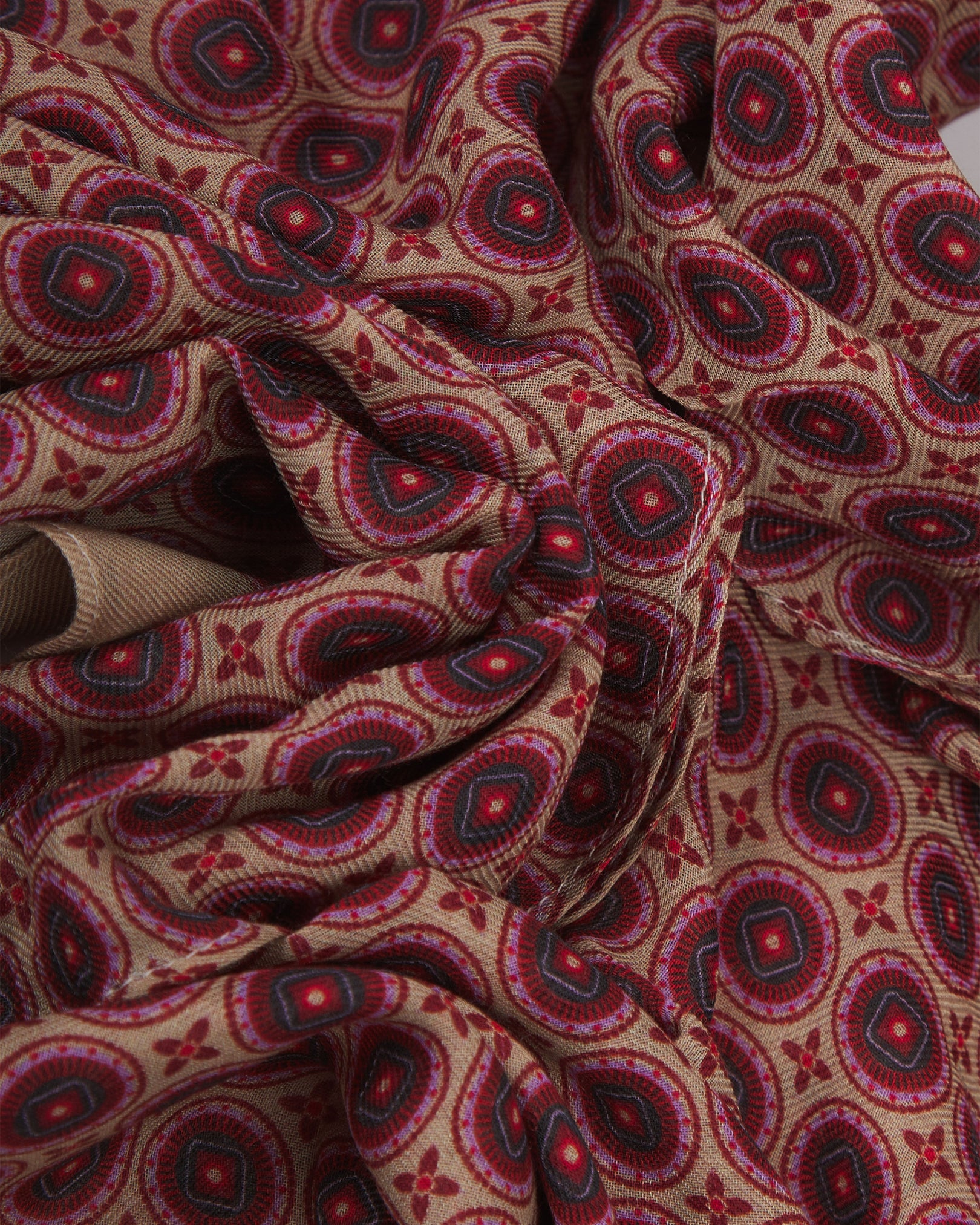 A ruffled close-up of the Bellingham 'Good Fortune' bohemian wide scarf, showing the soft modal and wool blend fabric with intricate concentric circular motifs in pink, red and maroon on a subtle cream background.