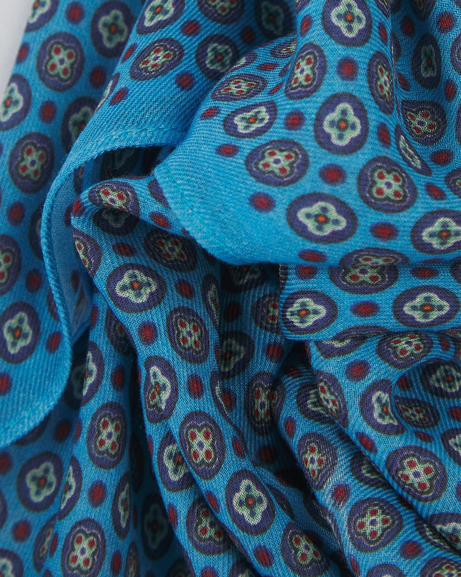 Close-up view of 'Toshima Gardenia' bandana. Ruffled and clearly showing the overlapping elements of multicoloured stylised floral patterns patterns against a blue background.