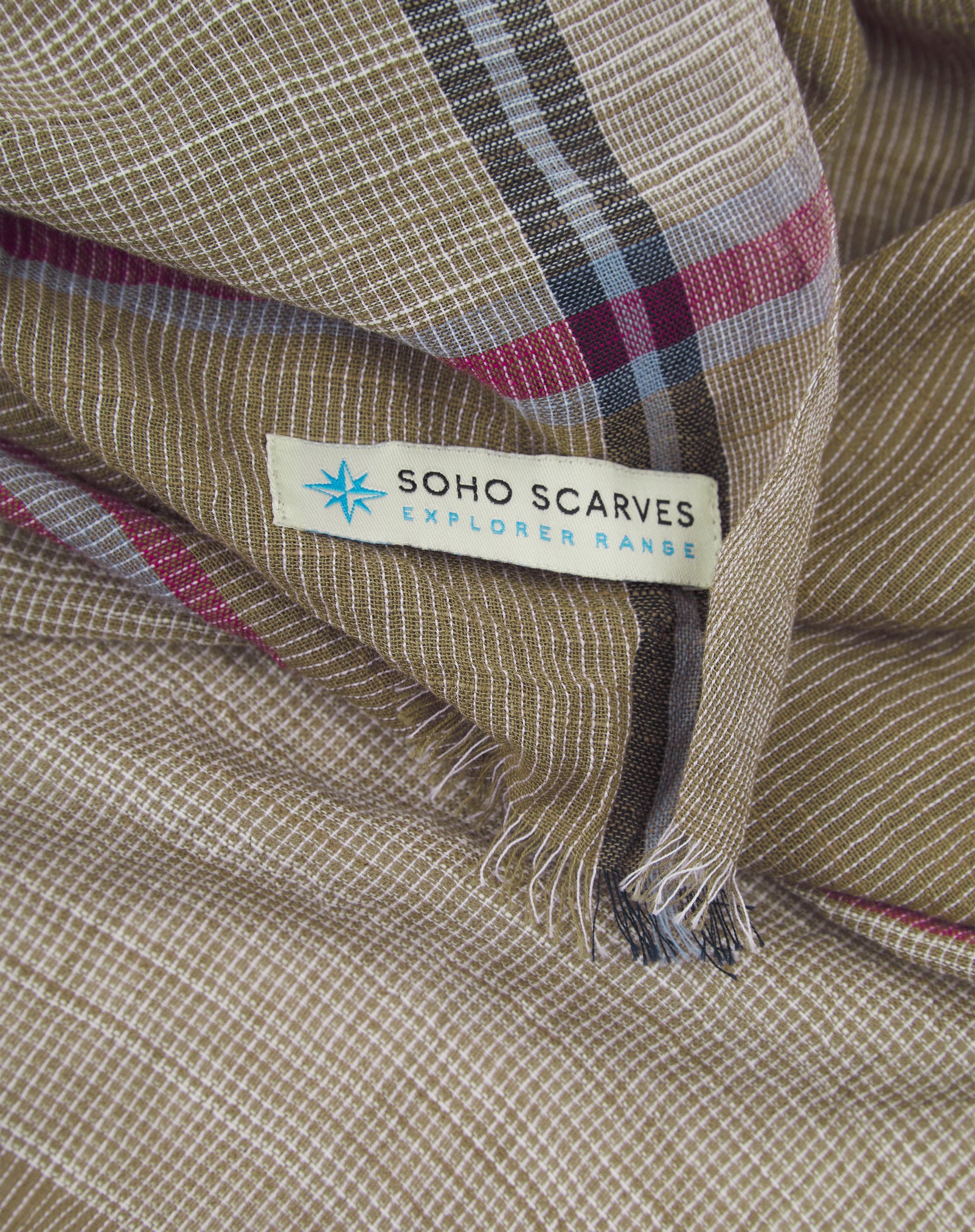 Ruffled close-up view of the pure cotton 'Attenborough' scarf, presenting a closer view of the tan, red and blue yarns which make up the loose striped pattern.