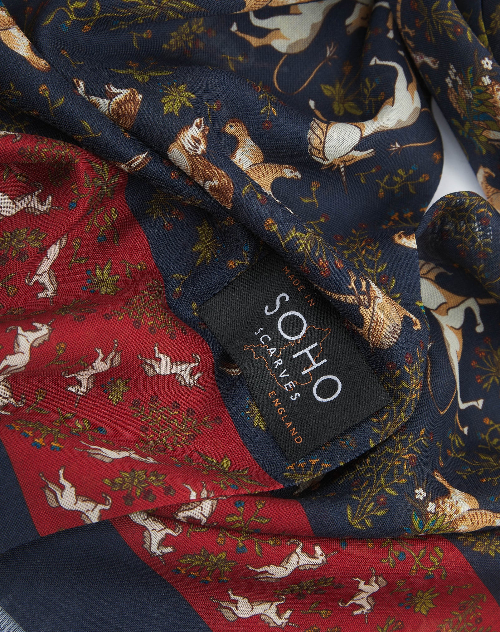 A ruffled, close-up view of the UK-made dark blue and rust-red silk and wool scarf depicting unicorns, hares and pheasants amid botanical forms. Clearly showing the premium silk and wool weave.