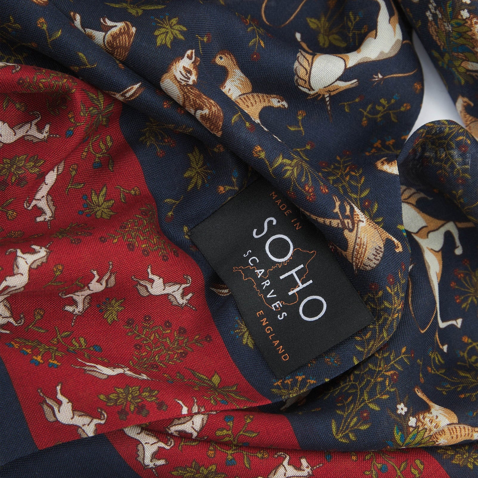 A ruffled, close-up view of the UK-made dark blue and rust-red silk and wool scarf depicting unicorns, hares and pheasants amid botanical forms. Clearly showing the premium silk and wool weave.