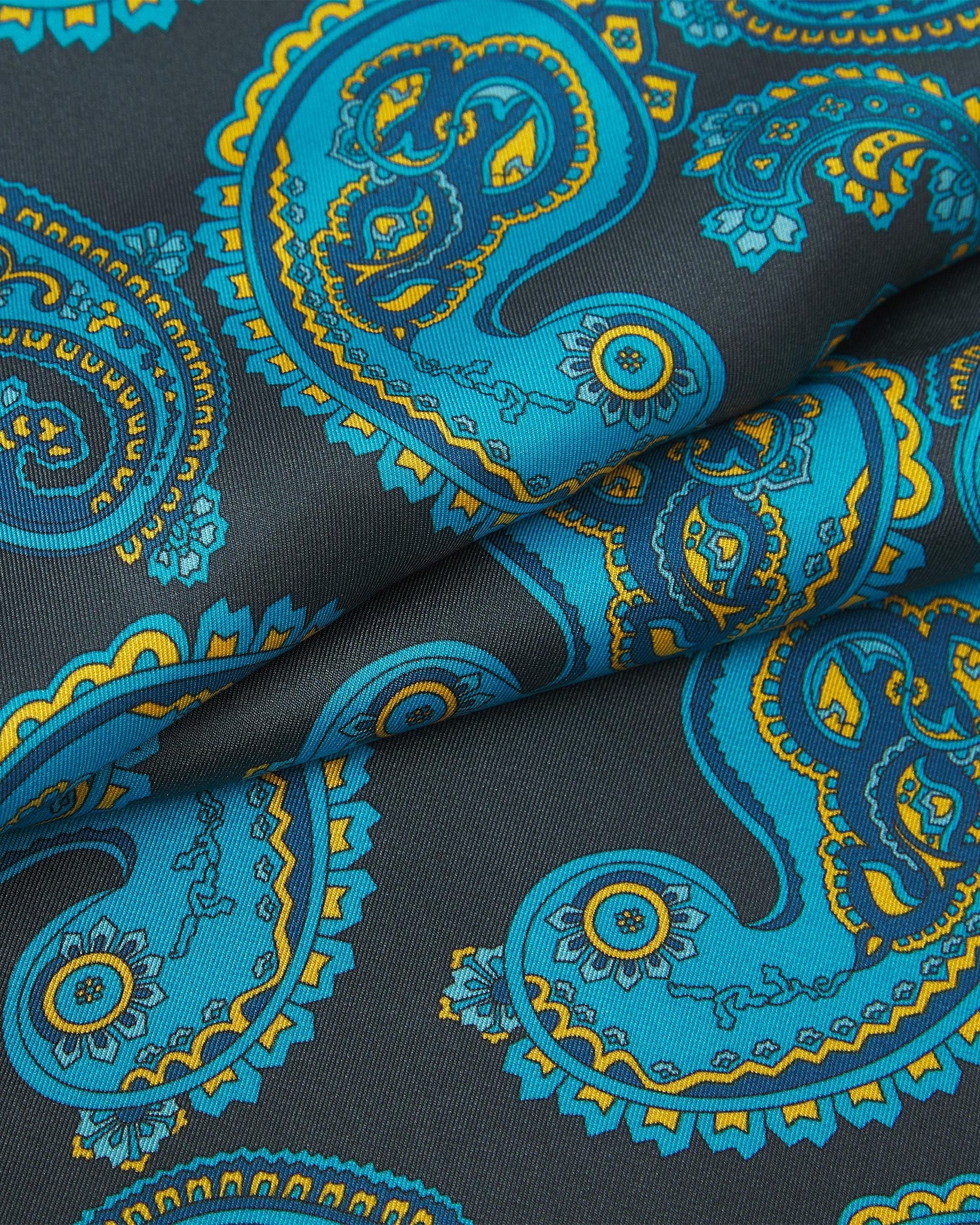 Ruffled close-up view of the Bridle silk scarf, presenting a closer view of the cyan paisley patterns with blue and gold accents against a dark grey background.