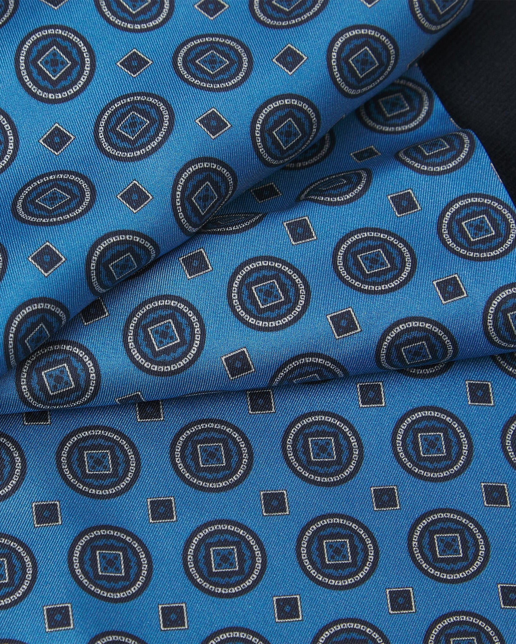 Ruffled close-up view of the Kyoto silk scarf, presenting a closer view of the symmetrical circle and square decorations against a vibrant blue background
