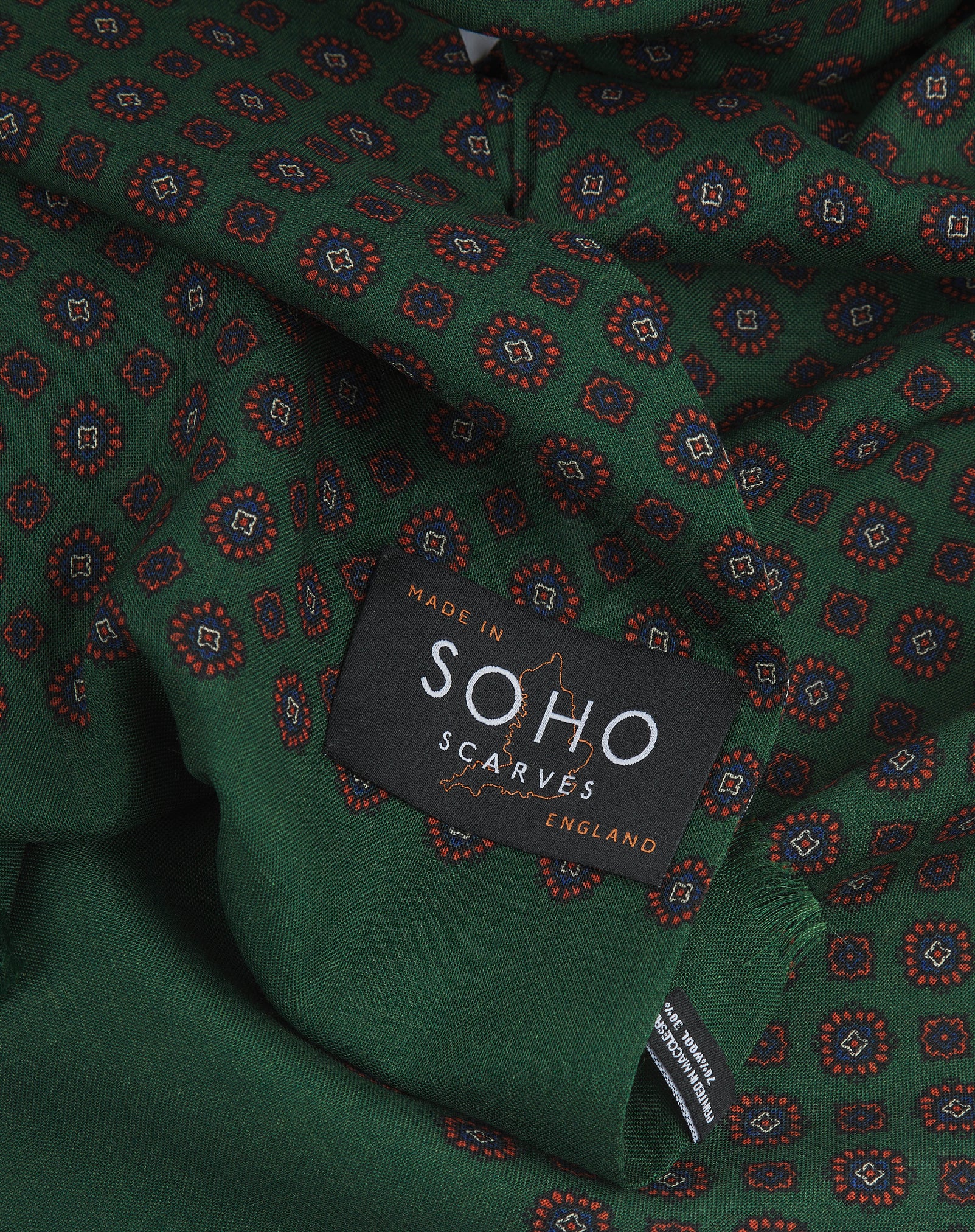 A ruffled, close-up view of the UK-made green and orange silk and wool scarf adorned with floral-inspired repeat patterns. Clearly showing the premium silk and wool weave.