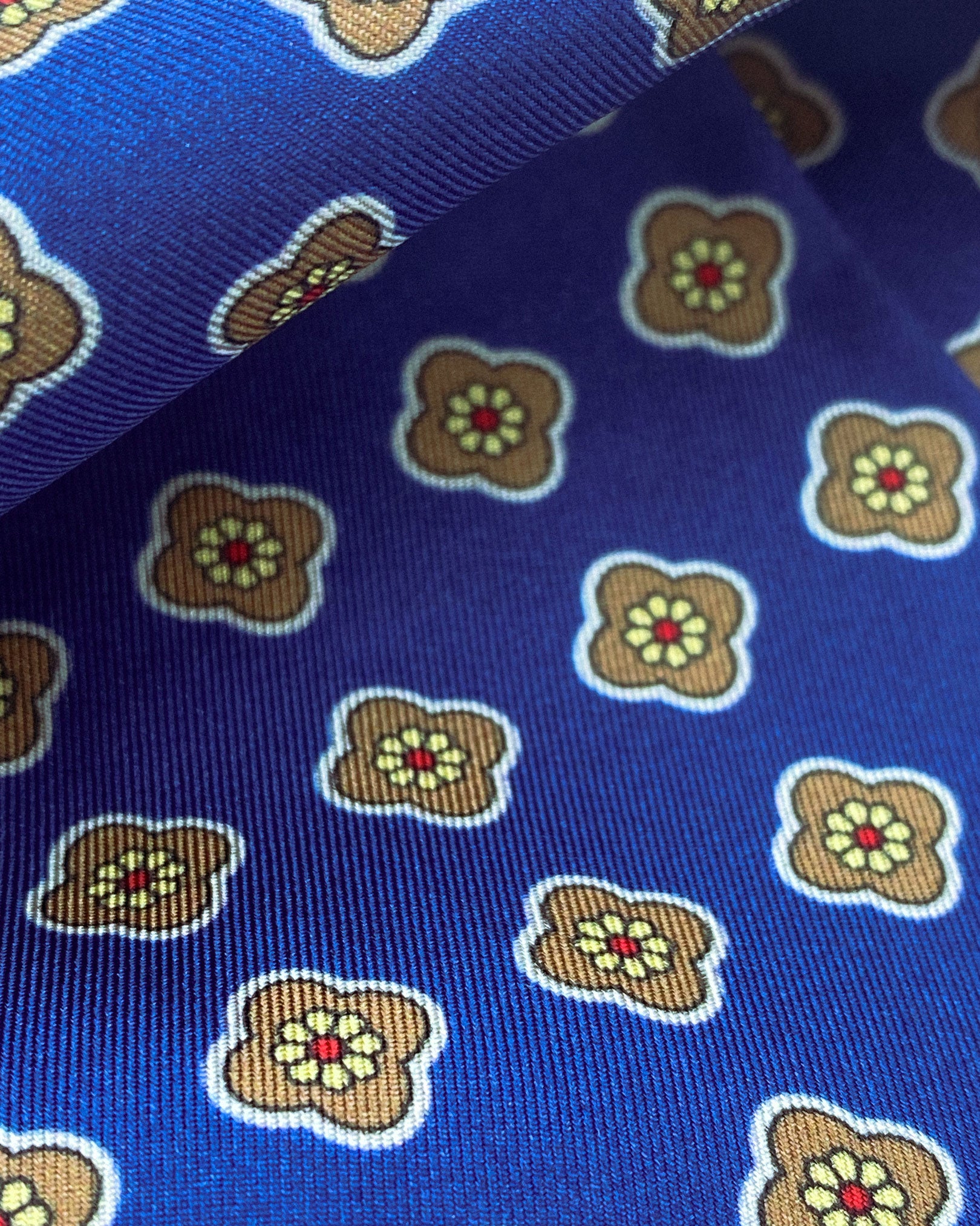 Ruffled close-up view of the Auburn silk aviator scarf, presenting a closer view of the pink flower patterns on a blue background and appealing lustre of the material.