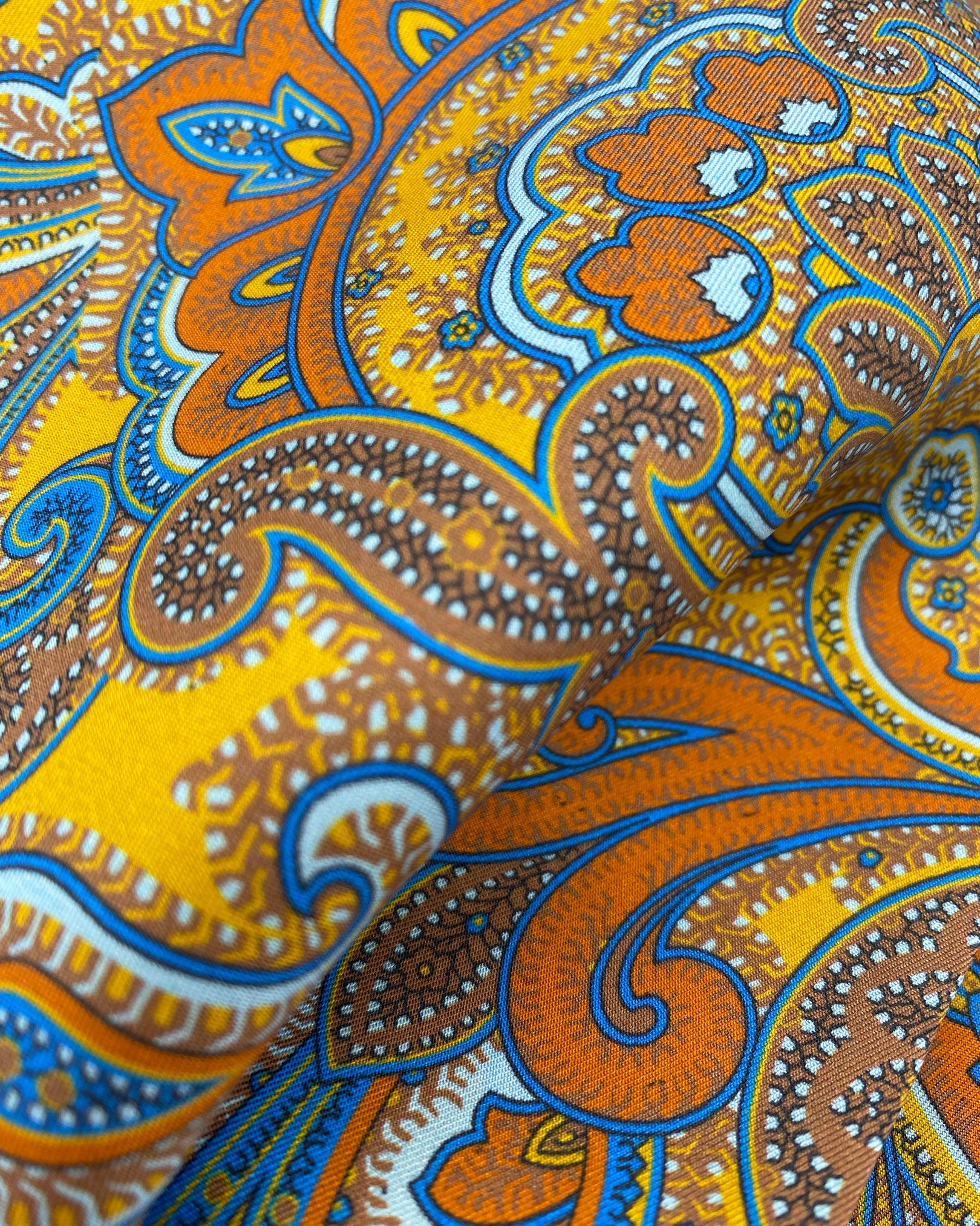 Ruffled close-up view of the 'Carnaby' silk scarf, presenting a closer view of the swirls of warm paisley tones against a bright golden ground and lustre of the silk material.