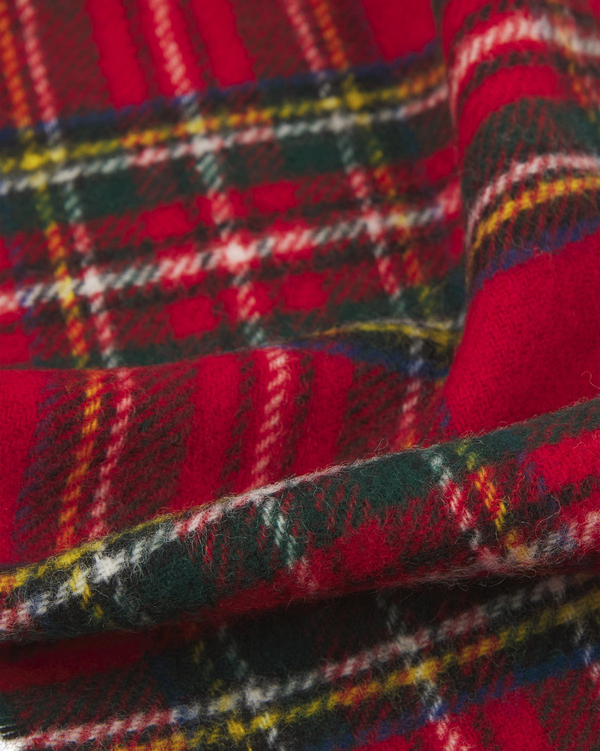 Ruffled close-up view of the UK-made, pure Merino wool 'Highlands' tartan in red scarf, presenting a closer view of the red, cream, blue, green, and yellow interlocking tartan pattern.