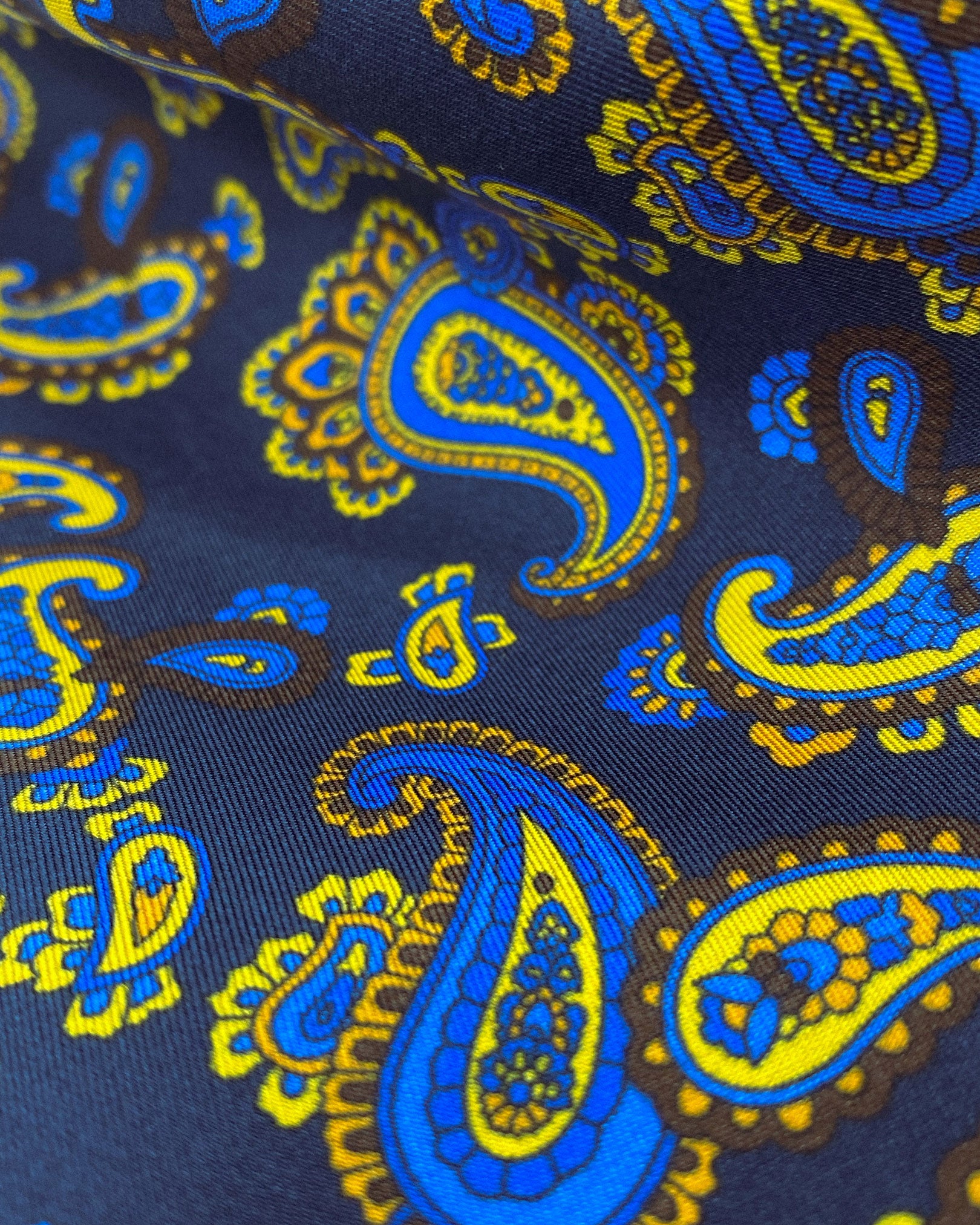 Ruffled close-up view of the Lucie silk aviator scarf, presenting a closer view of the intricate swirls of blue and yellow paisley.