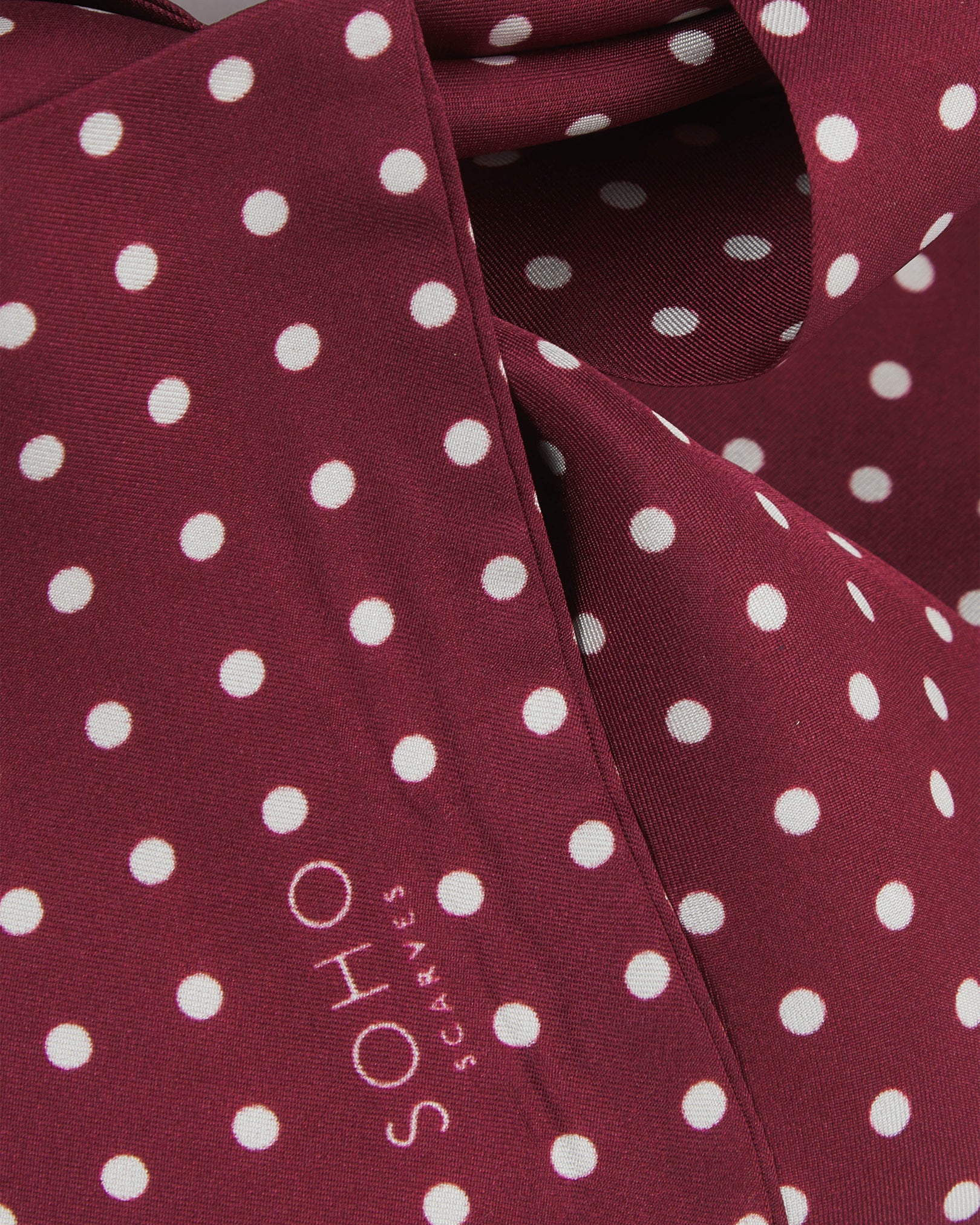 Ruffled close-up view of the Sapporo silk scarf, presenting a closer view of the polka dot design in deep maroon with white dots and appealing lustre of the material.