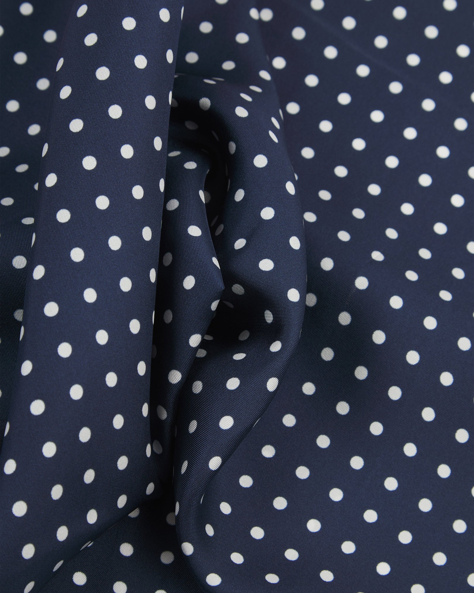 Ruffled close-up view of the 'Westminster' silk neckerchief, presenting a closer view of the polka dot design in navy-blue with white spots and subtle lustre of the material.