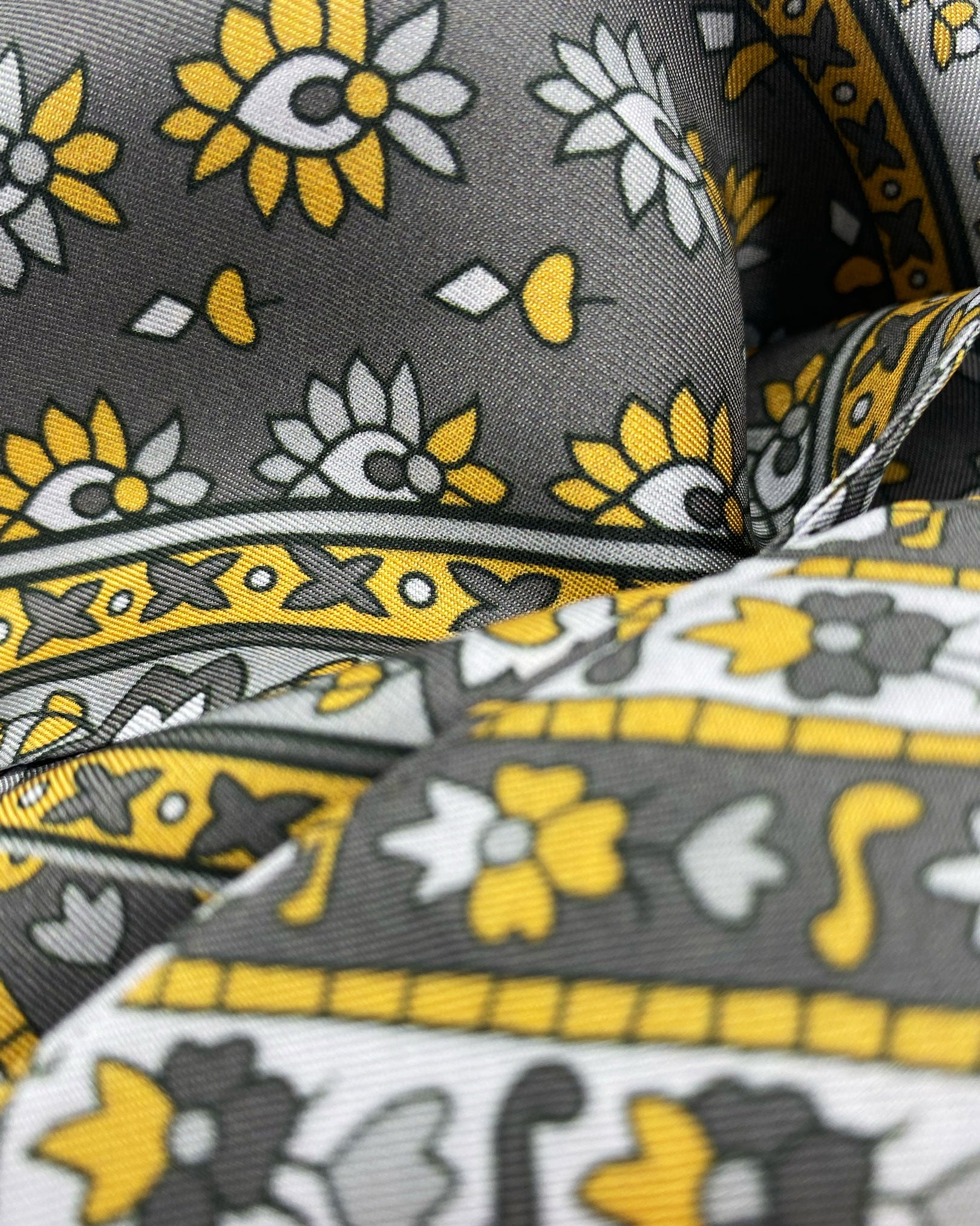 Ruffled close-up view of the Whitehorse polyester scarf, presenting a closer view of the floral and geometric circular and diamond patterns with silver, grey and muted yellow palette.