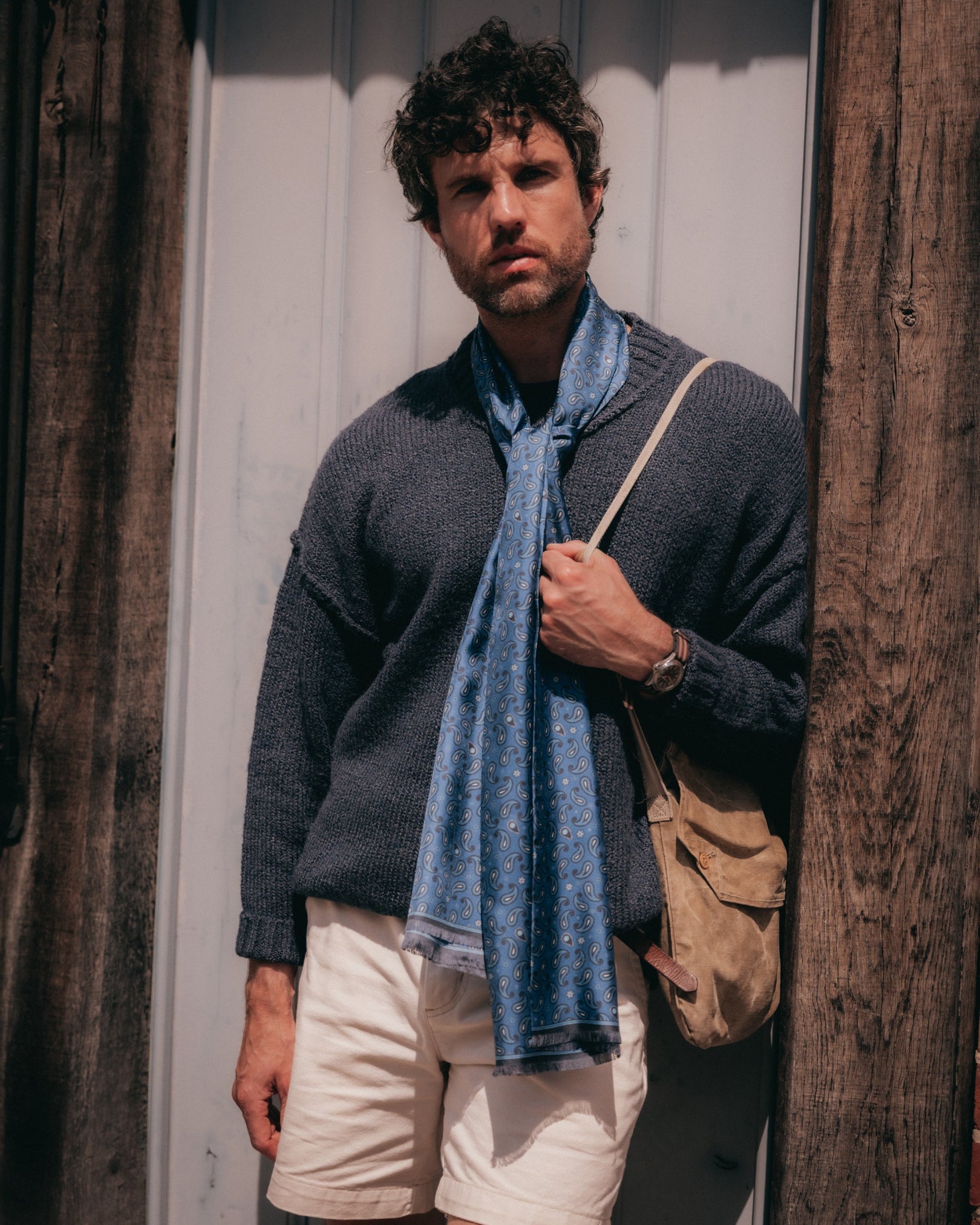 Man leaning against a doorway wearing the cornflower blue 'Highbury' silk scarf tied loosely around the neck.