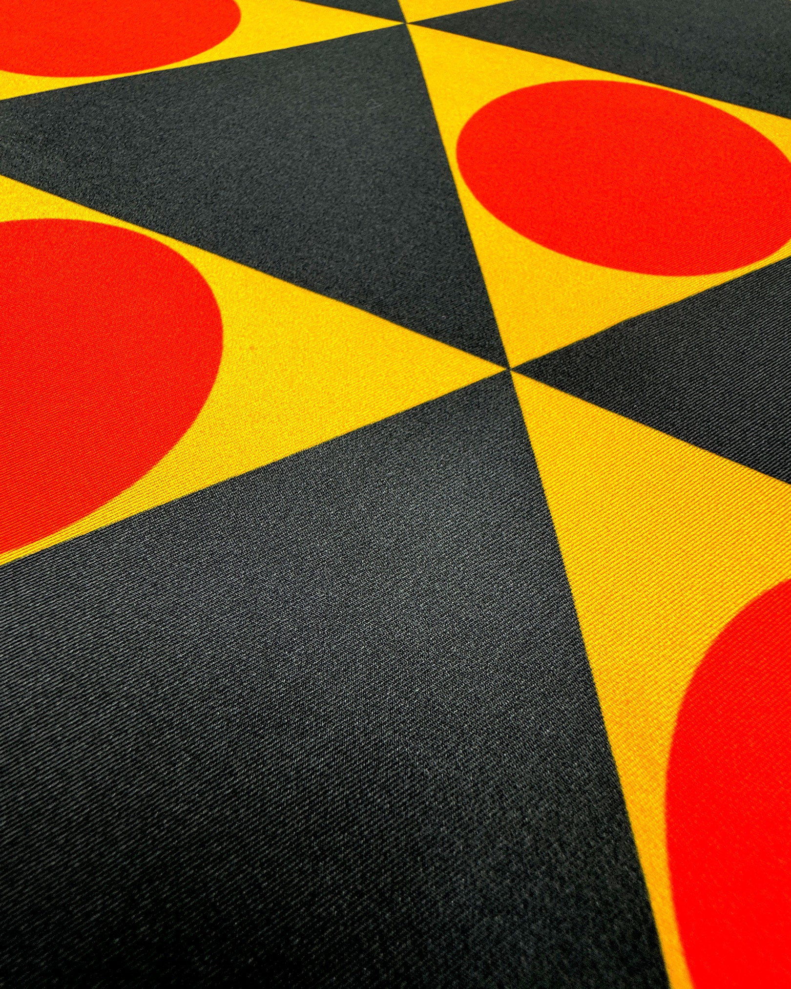 Close-up angled view of the bold yellow, charcoal and orange triangular and circular repeats of the 'Dresden' silk scarf.