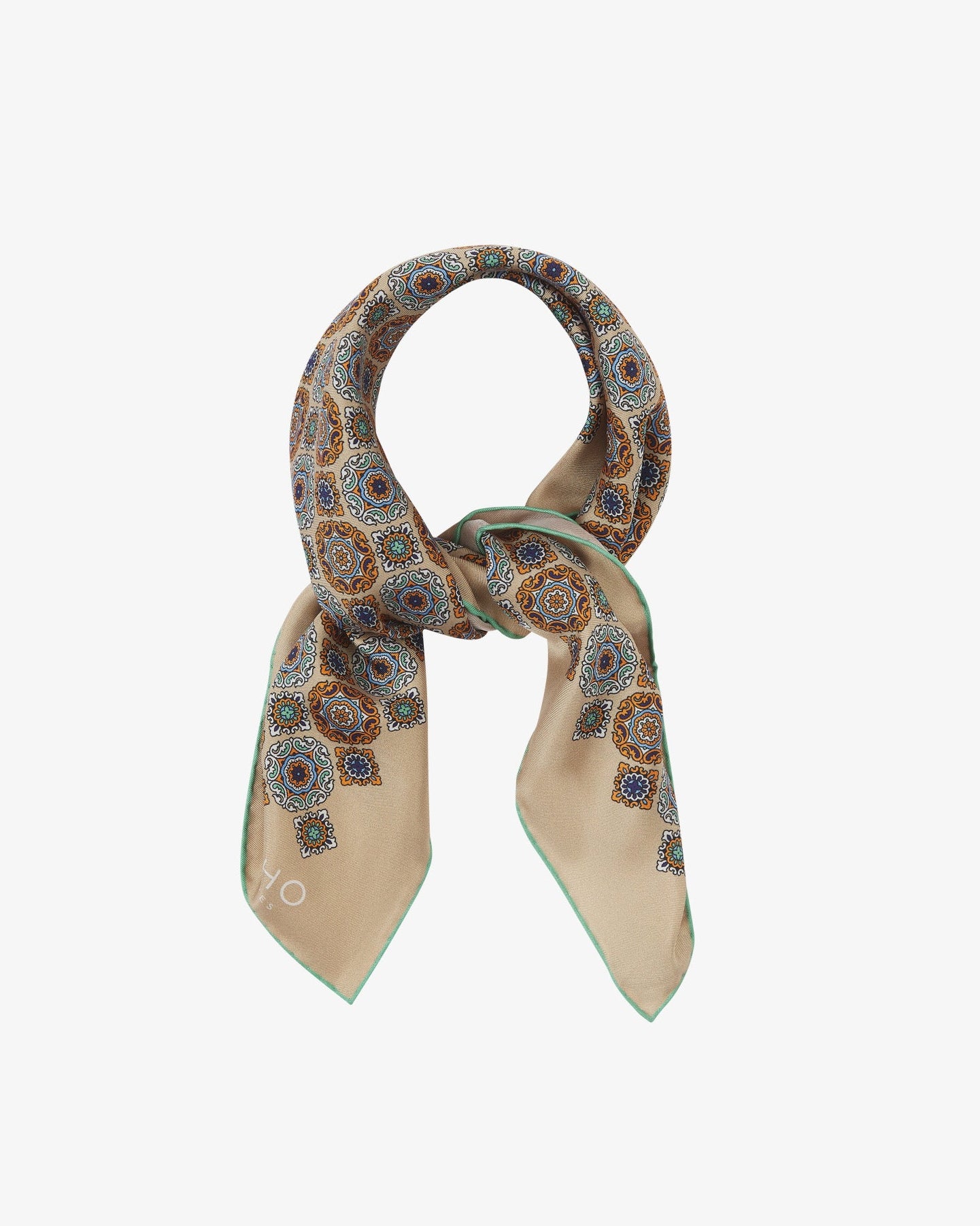 The 'Fitzrovia' neckerchief looped and knotted, revealing the ornate medallion design in navy, teal, and burnt orange against a warm hazelnut silk background.