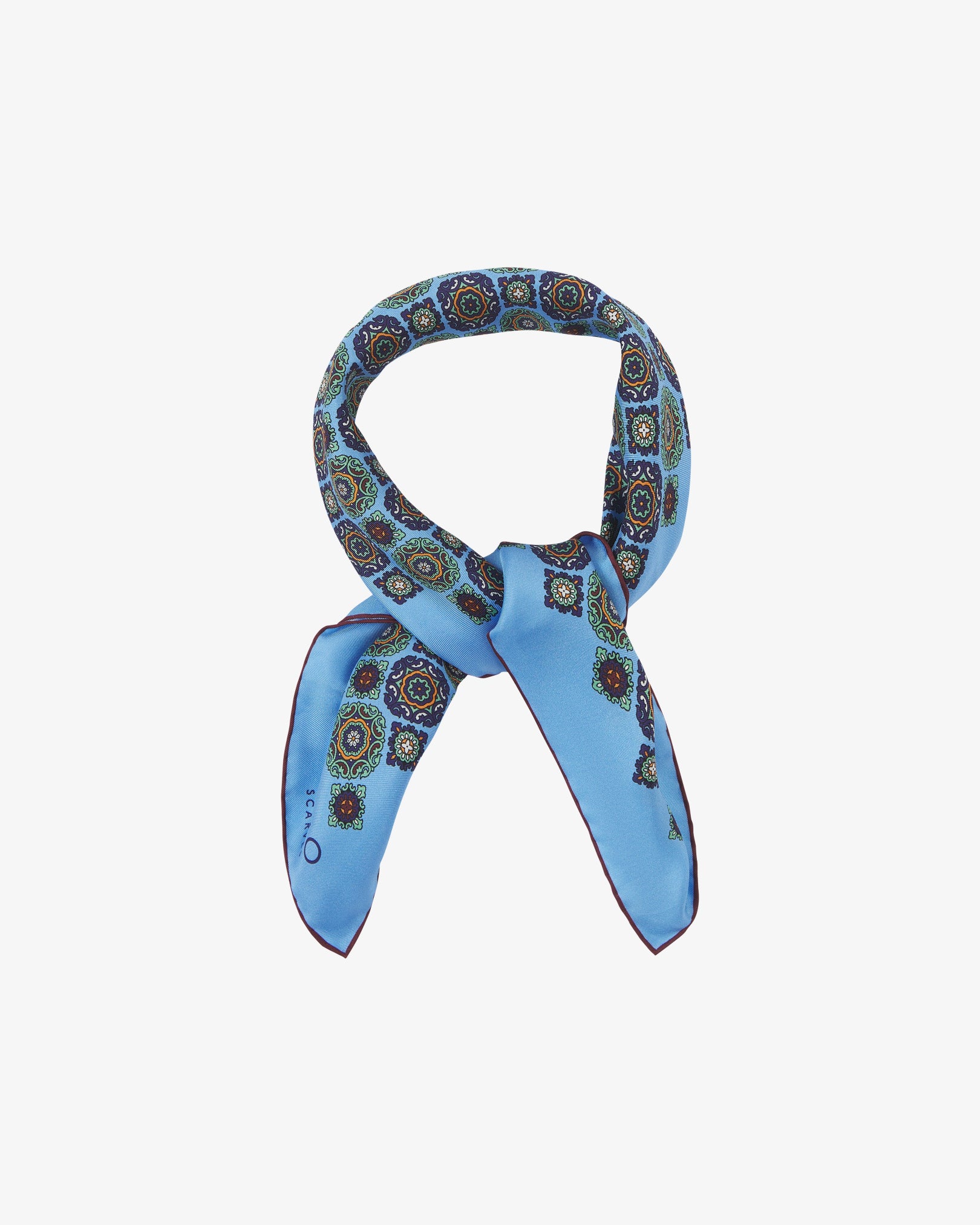 The 'Fitzrovia' neckerchief looped and knotted, revealing the bold medallion motifs in navy, forest green, and ochre against a cool Leyland blue silk.