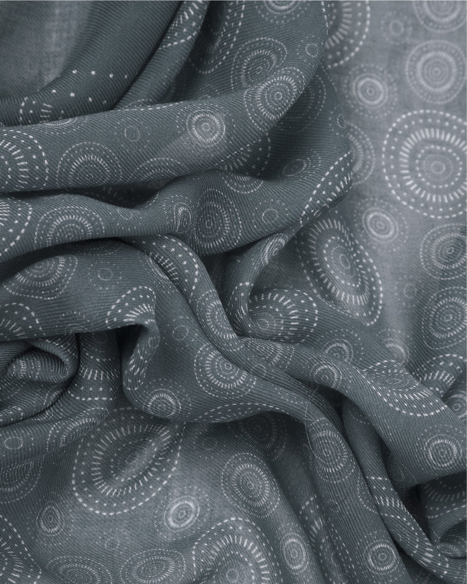 A ruffled close-up of the 'Circles in Graphite' modal and wool bandana from SOHO Scarves, highlighting the soft modal and wool blend fabric with concentric Op art-inspired disc motifs formed from tiny contrasting dots in graphite grey tones.