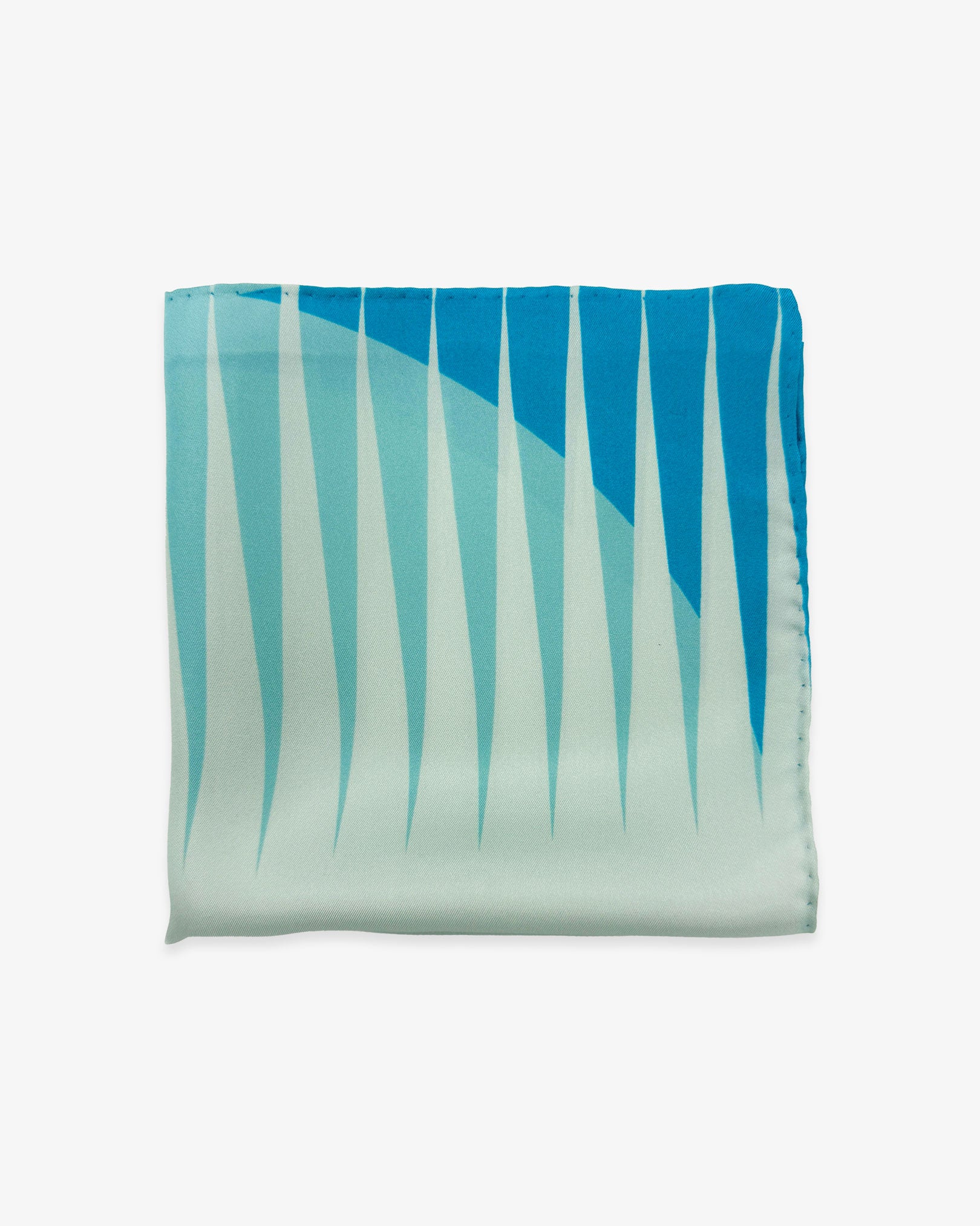 The 'Hamburg' silk pocket square from SOHO Scarves folded into a quarter, showing a portion of the bauhaus-inspired triangular and circular forms in a cool palette.