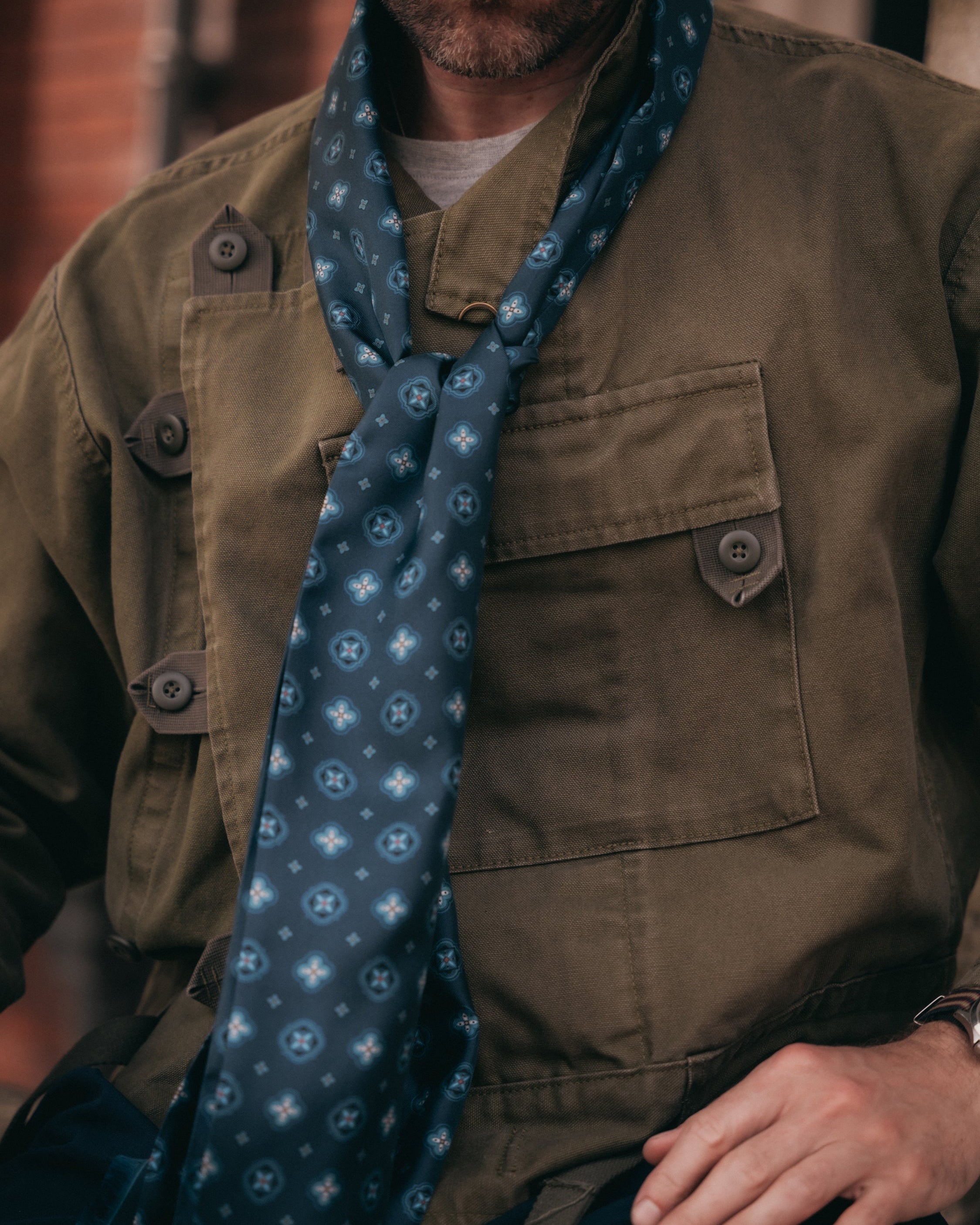 Close-up view of man wearing the indigo 'Chelsea' silk scarf from SOHO Scarves with a clear view of the patterns comprising of pale teal cross motifs and circle medallions.