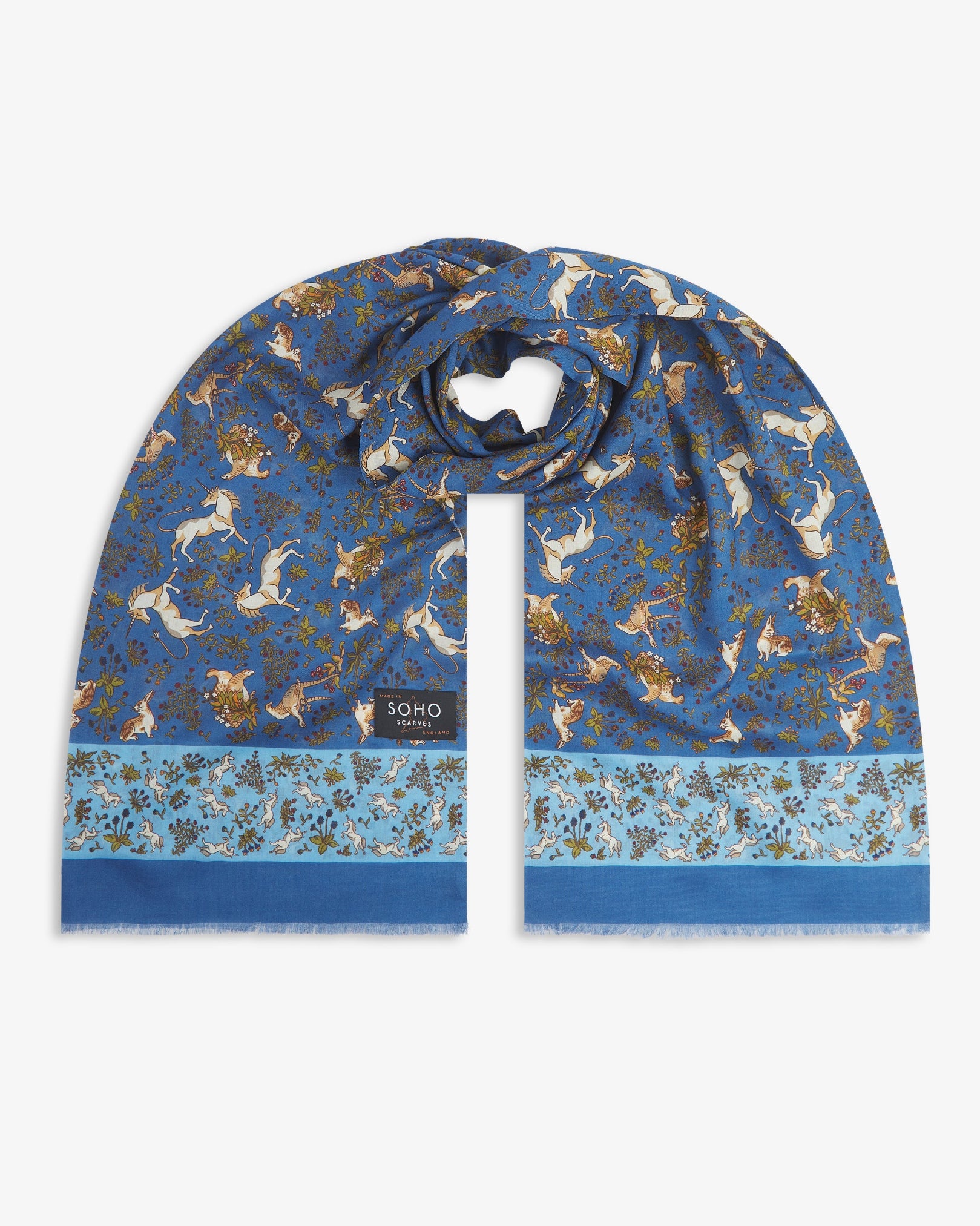 Premium blue silk-wool scarf depicting animals amid botanical forms. Unravelled and looped in the middle, presenting slightly longer and wider scarf dimensions, ornate border and 'Soho Scarves' label.