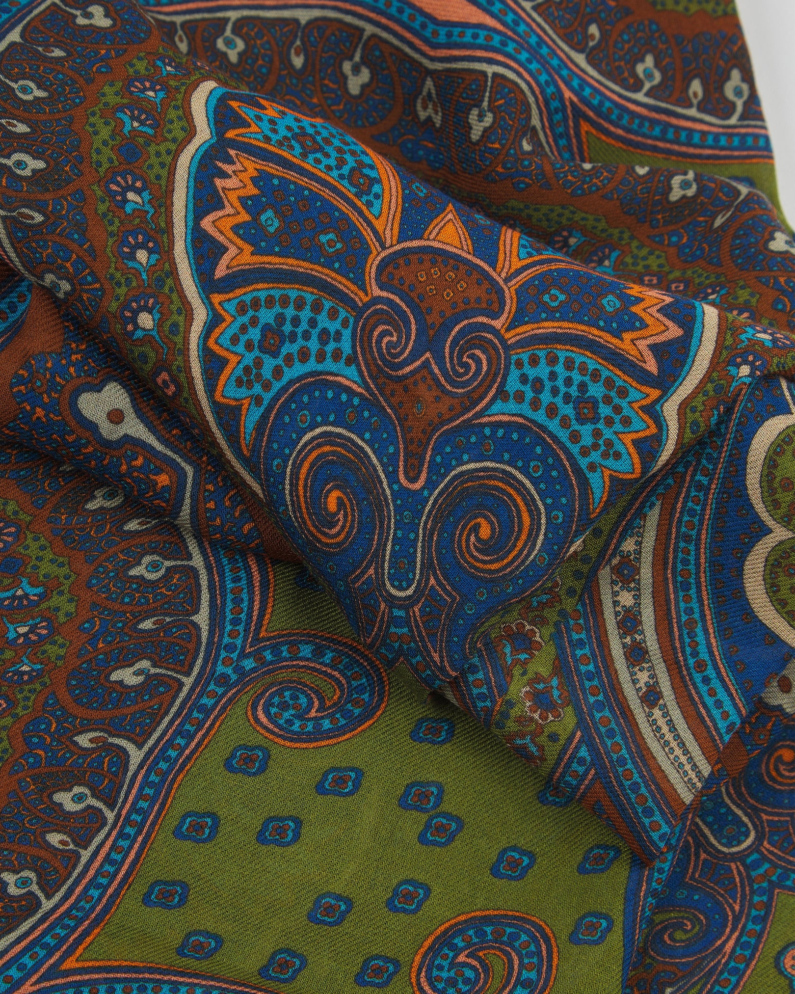 A ruffled close-up of The Montreal bohemian wide scarf, highlighting the soft modal and wool blend fabric with intricate abstract paisley-inspired patterns in rich earthy tones of olive green, brown, blue and burnt orange.