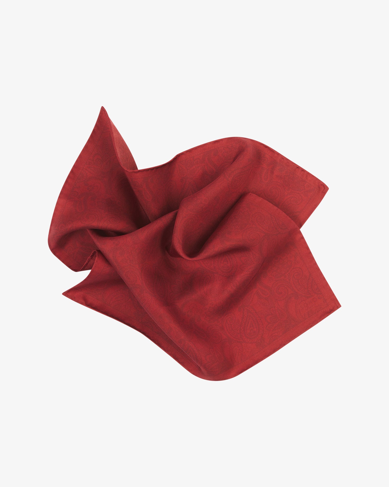 The cranberry silk pocket square twisted in the middle, highlighting the sheen and delicate texture of the paisley-patterned silk.