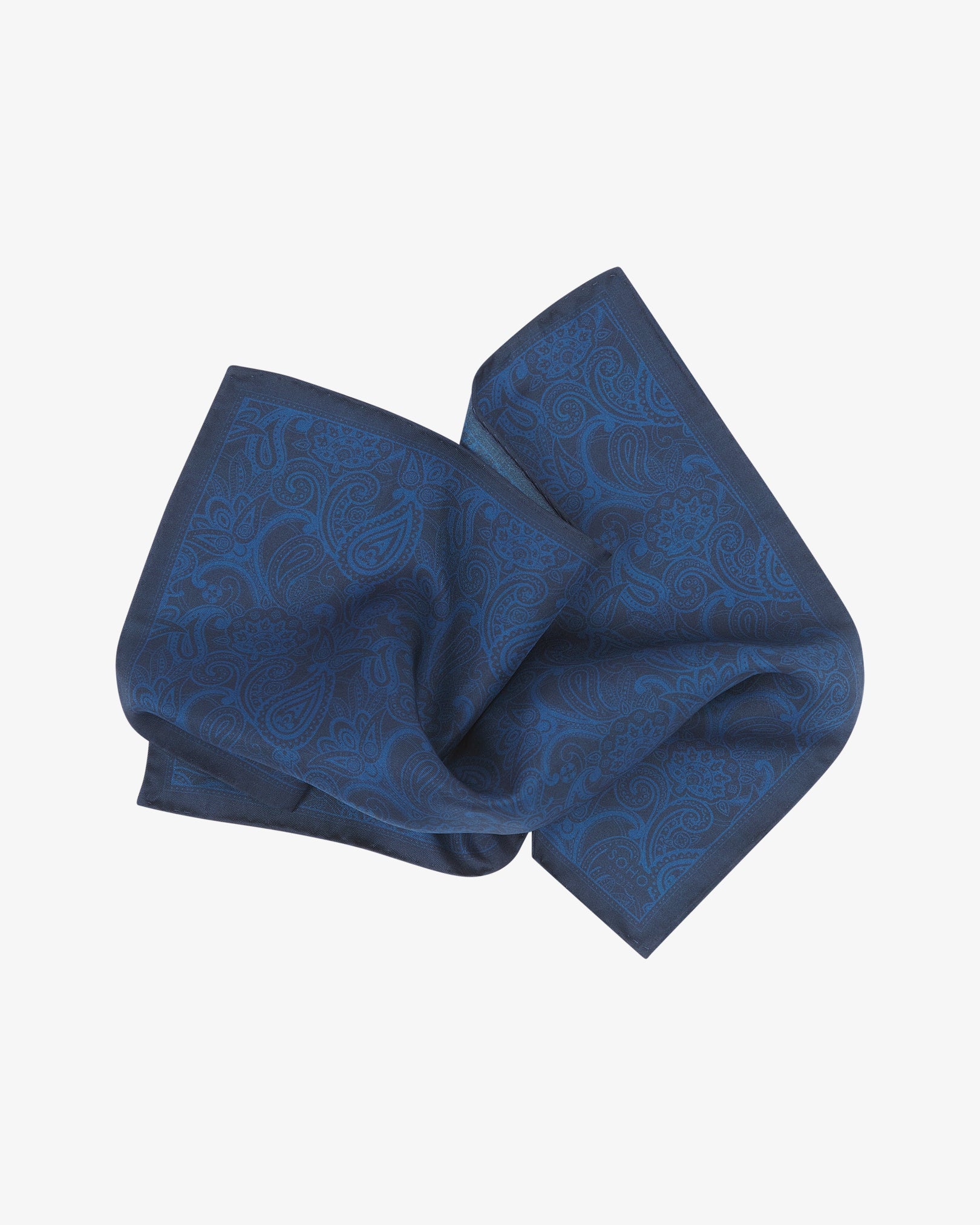 The dark navy silk pocket square twisted in the middle, highlighting the subtle sheen and fine weave of the paisley-patterned silk.