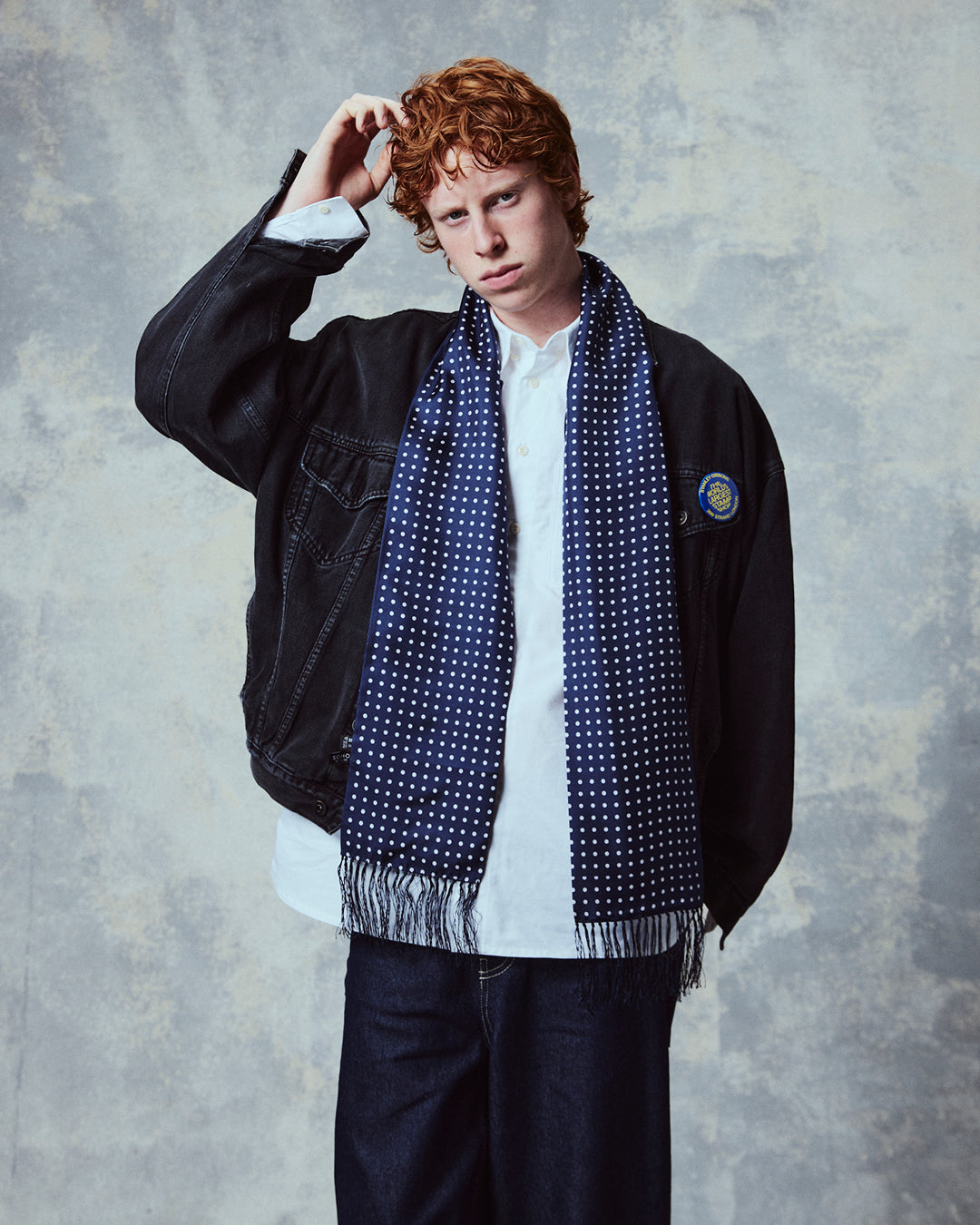 Demonstration of man wearing the 'Westminster' polka dot silk aviator scarf from Soho Scarves in navy blue.