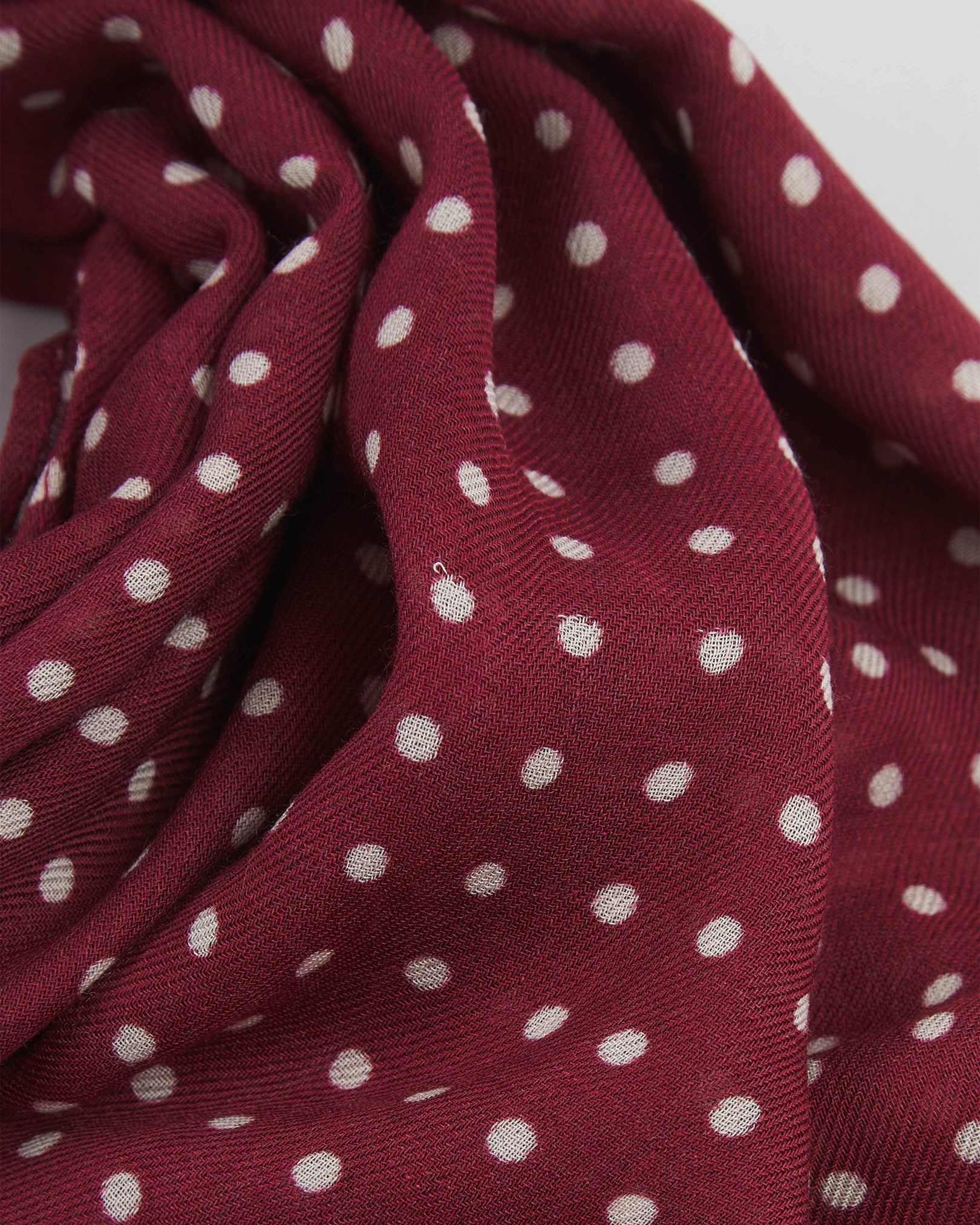 A ruffled close-up of The Sapporo bohemian wide scarf, showing the soft modal and wool blend fabric with evenly spaced white polka dots on a maroon background.