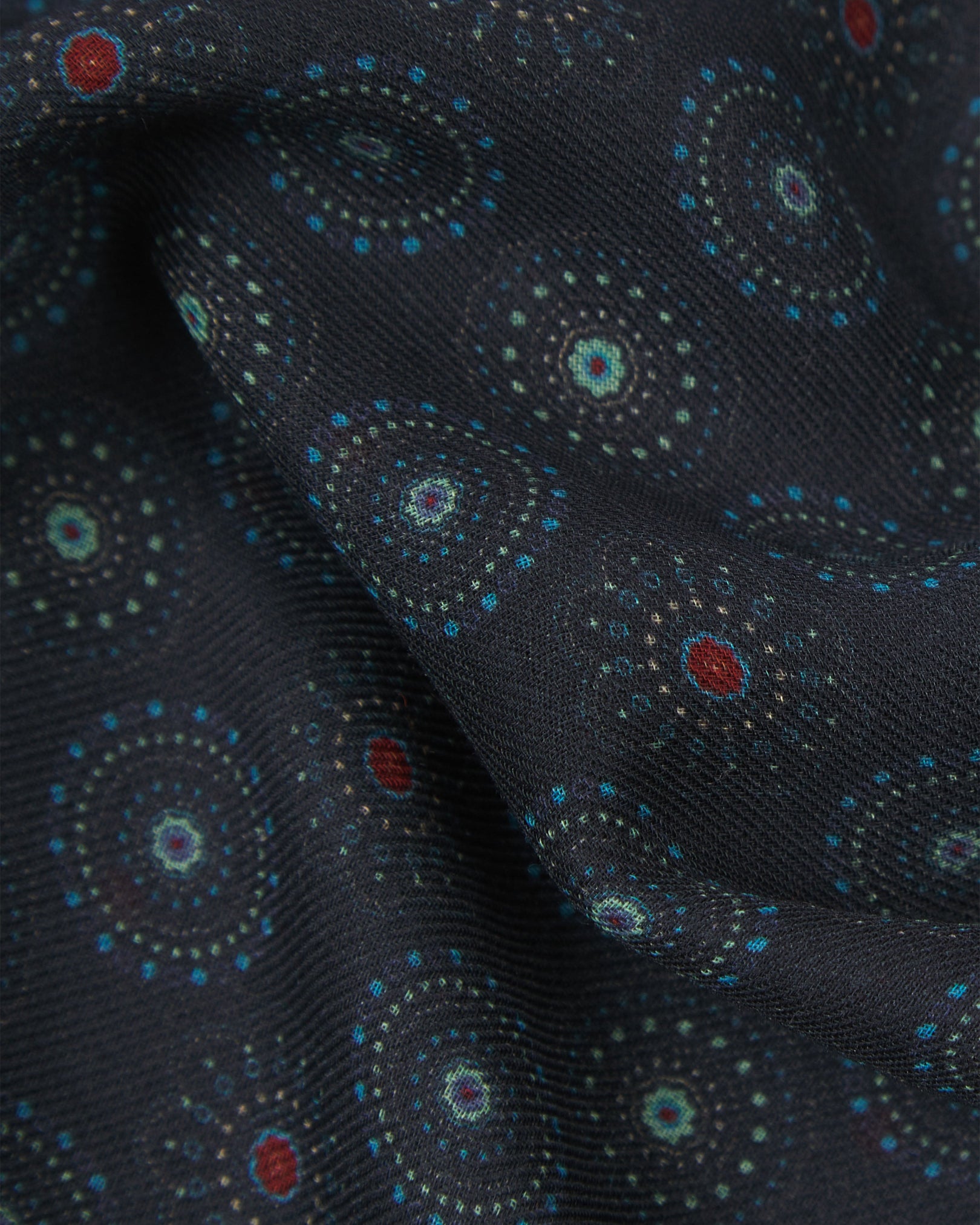 A ruffled close-up of the Seattle 'Gardenia' bohemian wide scarf, showing the soft modal and wool blend fabric with intricate circular motifs in blue and mint green on a black background with subtle red accents.