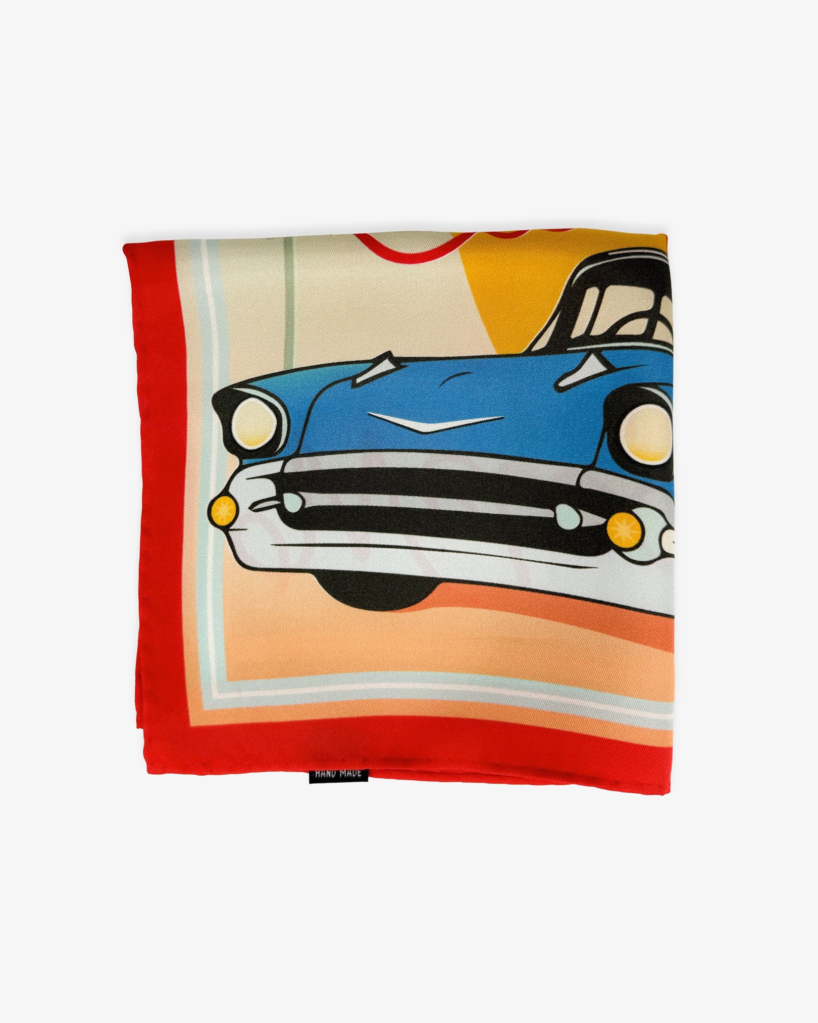 The 'Sunset Ride' blue silk pocket square from SOHO Scarves folded into a quarter, showing a portion of the blue Cadillac and red border.