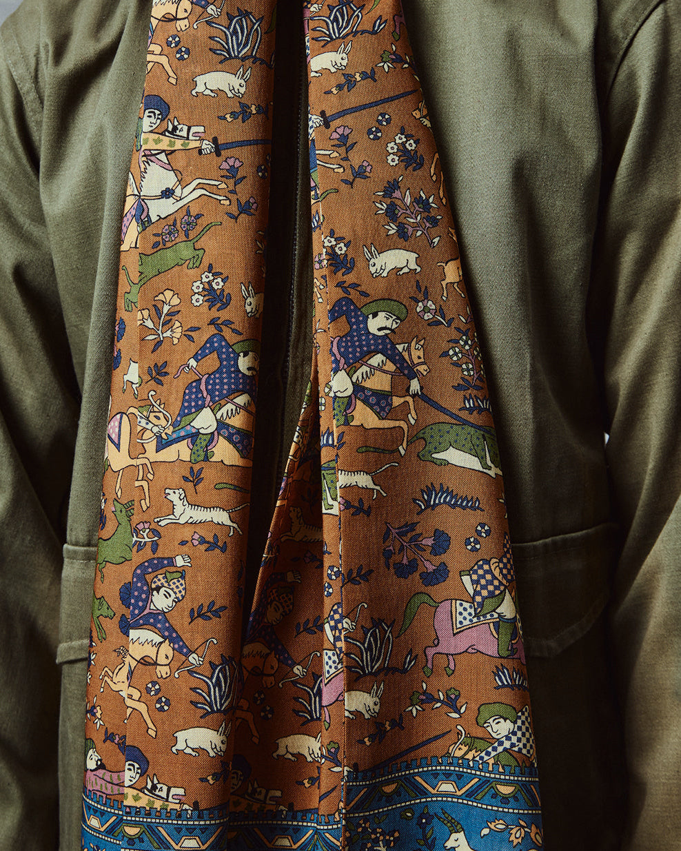 Close-up wearing the English-made, 'Hunters in Dull Gold' silk and wool scarf, with focus on the multicoloured design on a dull gold ground, combining ancient East Asian hunting motifs.