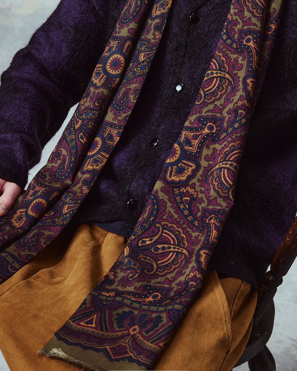 Seated wearing the English-made, 'Paisley in Highland Green' silk and wool scarf, with focus on the highland green, red and gold design.