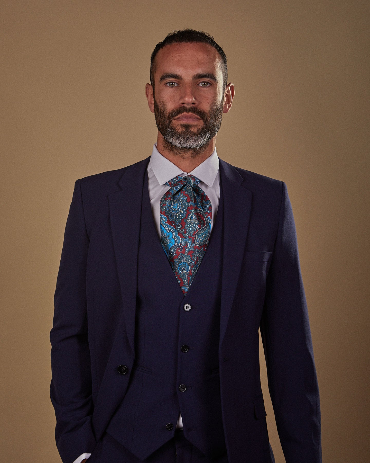 Front view wearing a 'Dean' silk Double Ascot tie from SOHO Scarves, paired with white shirt and three-piece midnight blue suit. Tie is worn quite tightly to neck and neatly tucked under waistcoat.