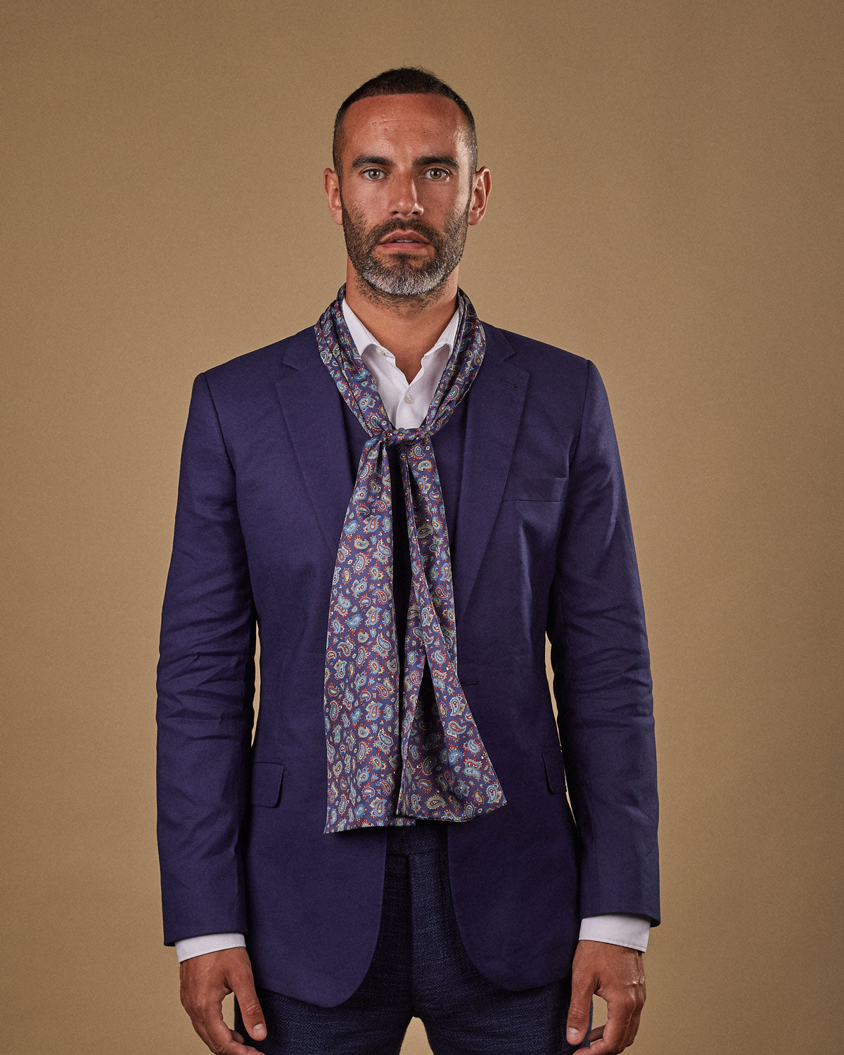 Portrait view of male model wearing 'The Lexington' silk scarf. Tied loosely around neck in a simple knot and shoulders and paired with a smart, midnight-blue suit.