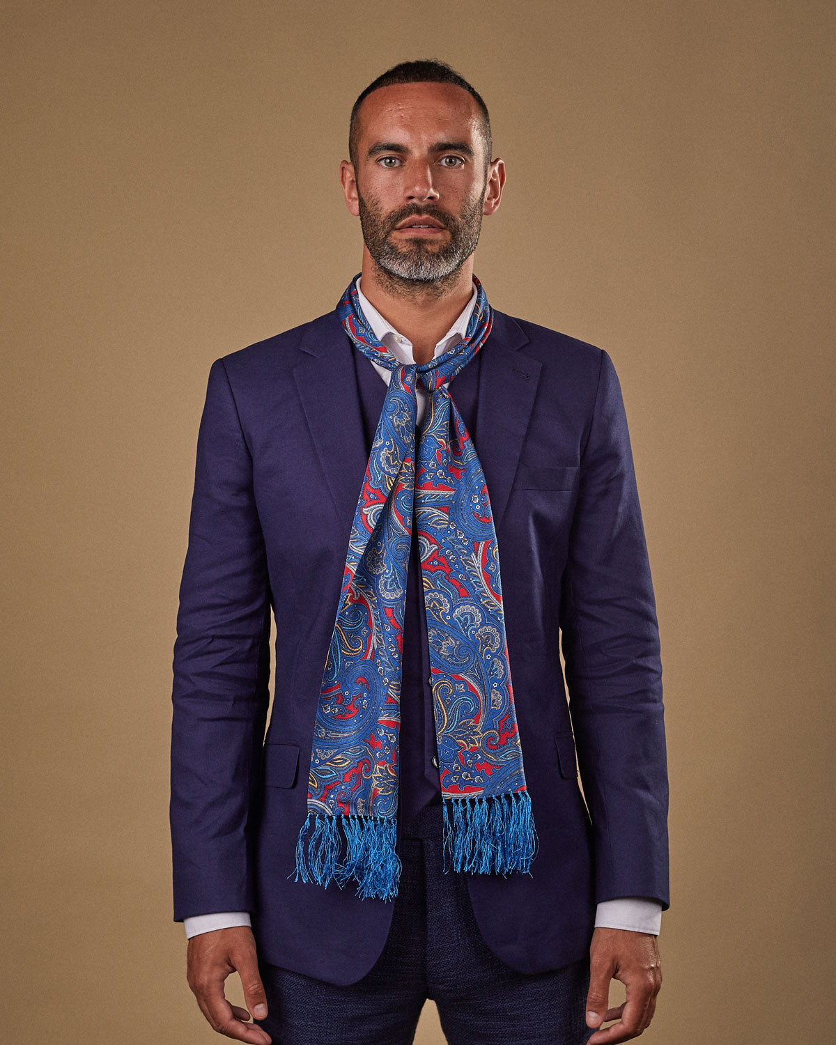 Portrait view of male model wearing 'The Oxford' silk aviator scarf. Tied loosely around neck in a simple knot and shoulders and paired with a smart, midnight-blue suit.