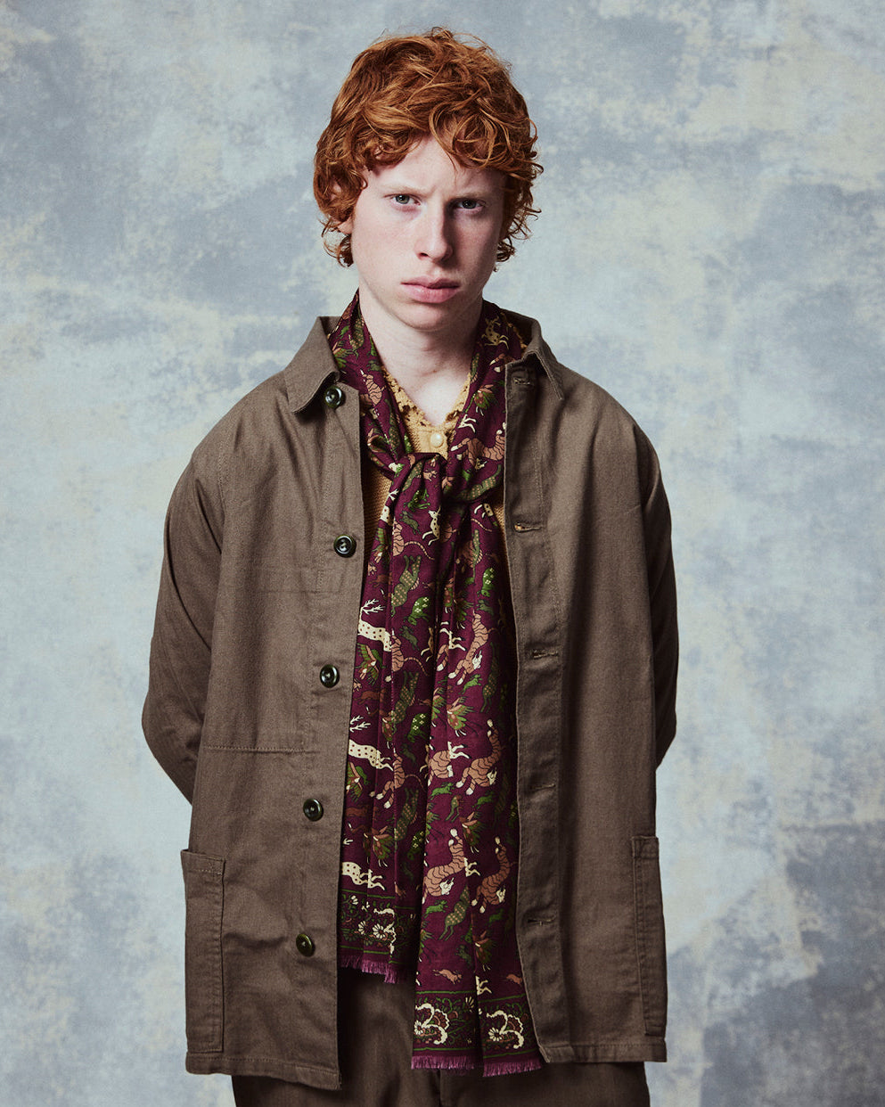 Top-half view of man wearing the English-made, 'Woodland Creatures in Burgundy' silk and wool scarf from Soho Scarves.