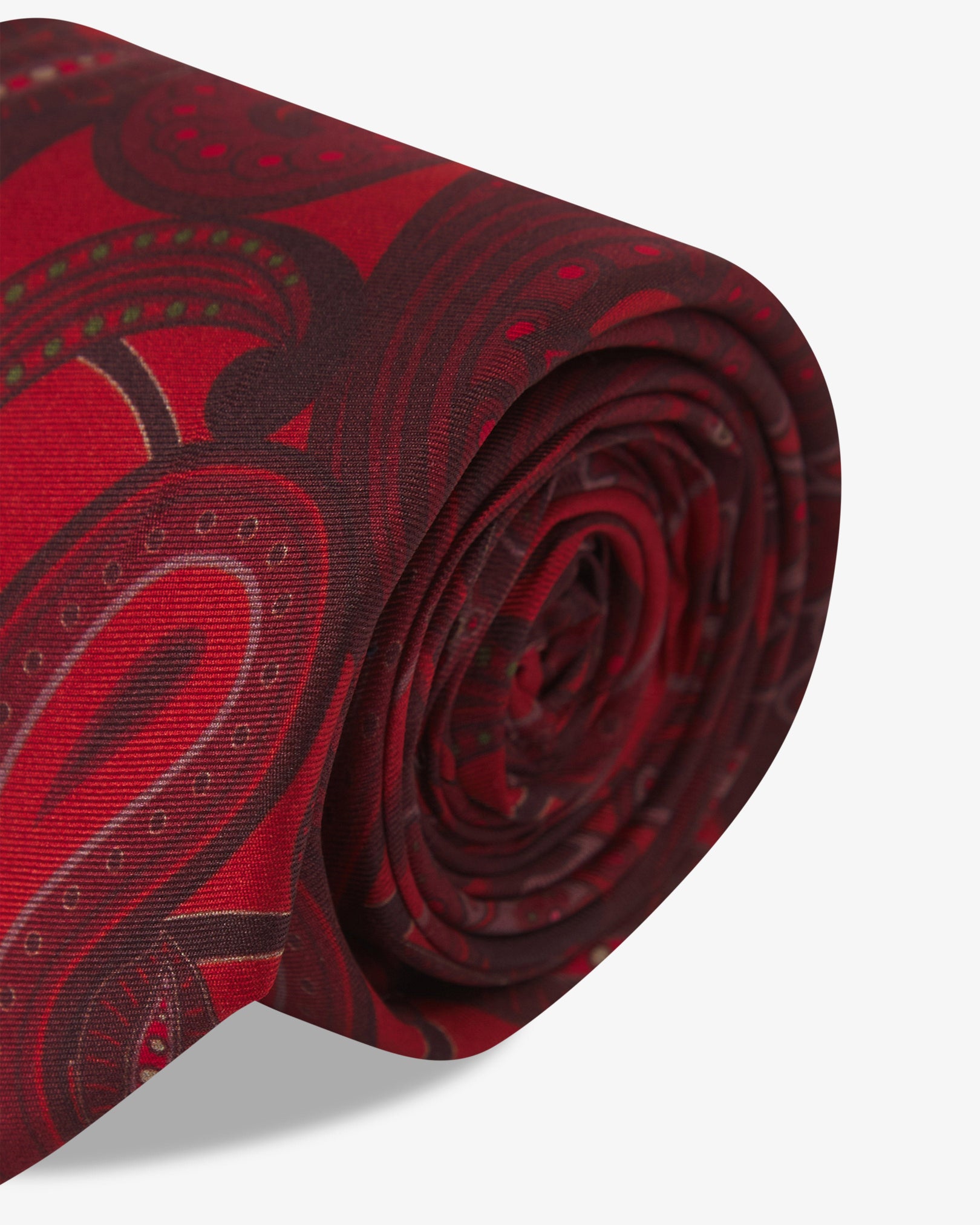 The 'Windermere Good Fortune' silk neck tie neatly coiled with a clear view of the dark red paisley patterns against a rich red ground.