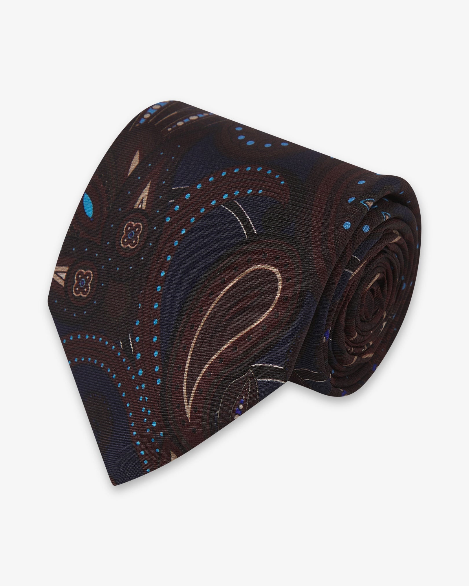 Focus on the tip of the 'Windermere Mahogany Haze' silk neck tie. Showing the brown paisley motifs and the remaining tie length neatly coiled.