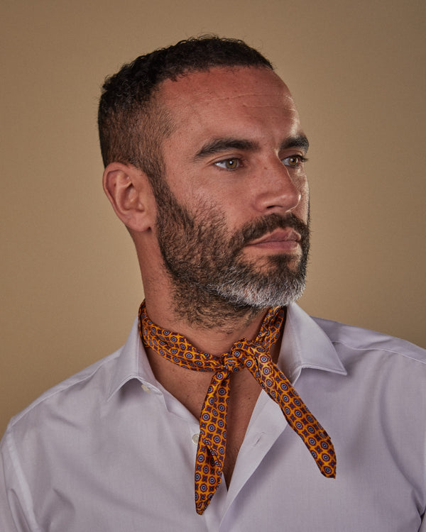 Head and shoulders view of model facing slightly to his left, wearing the ‘Toshima’ silk neckerchief with knot tie at front and paired with white shirt.