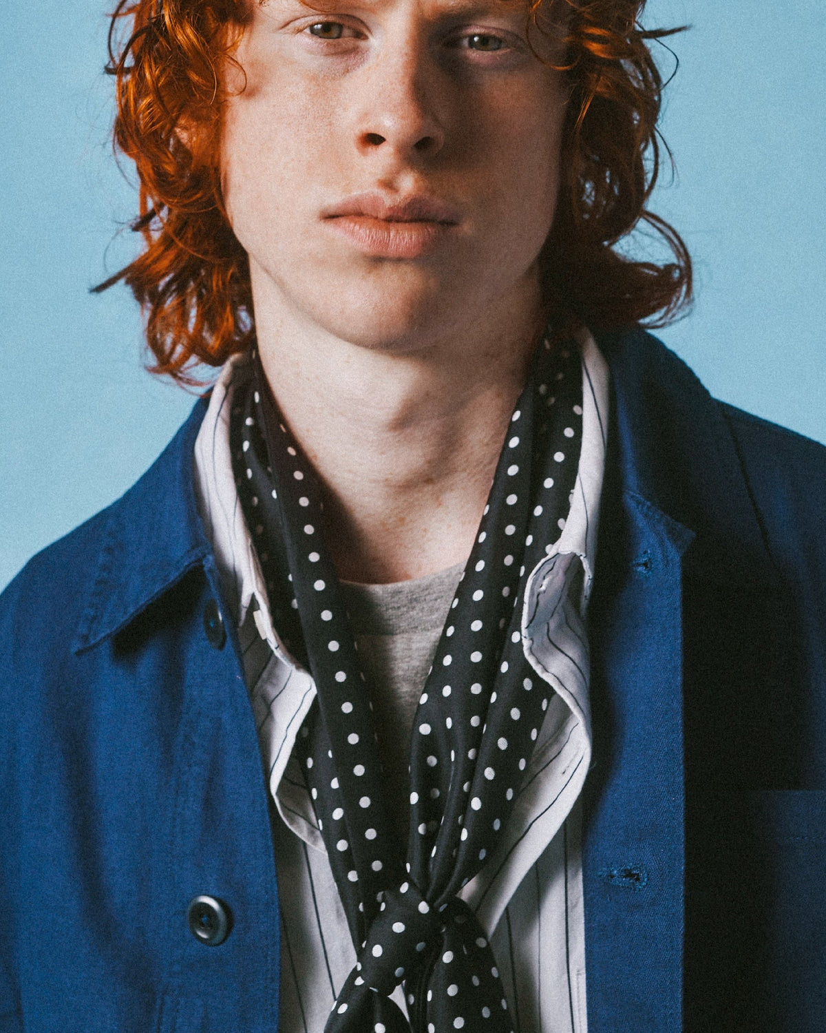 A person with red hair wearing a blue jacket over a white shirt and a black-and-white polka dot scarf, photographed against a light blue background. The text 'SOHO SCARVES' appears at top left, with 'CLASS OF 2023' and 'THE SHINAGAWA SILK SCARF' at the bottom.