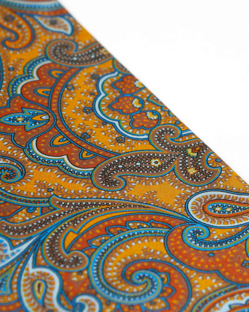 Angled view of the luxury deep gold scarf, focussing on the deep orange, light blue and brown paisley patterns.