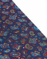 Angled view of the small light blue, gold and white paisley patterns on the beautiful deep blue scarf.