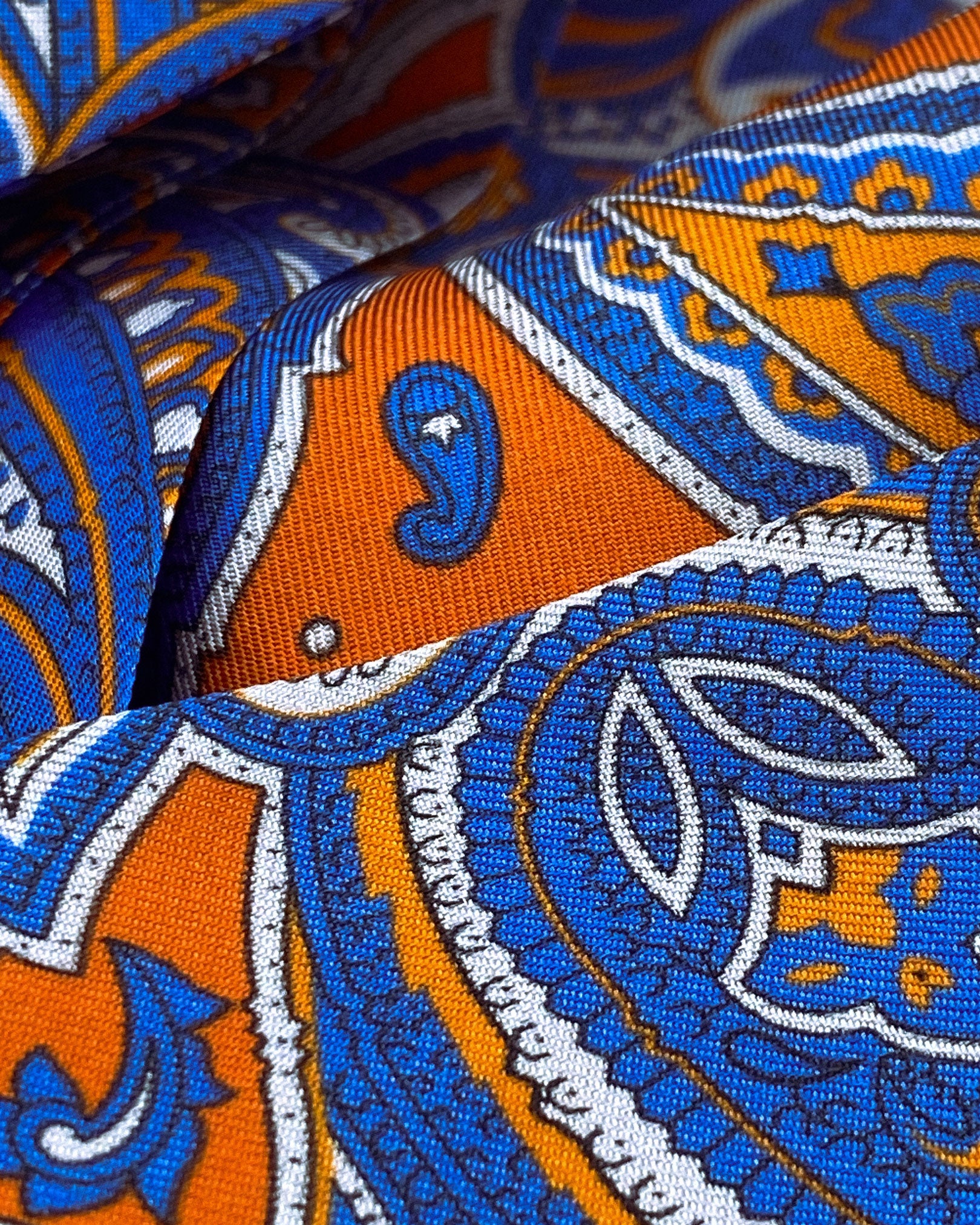 Angled and ruffled close-up view of the blue and orange paisley patterns of the silk Orlando Aviator.