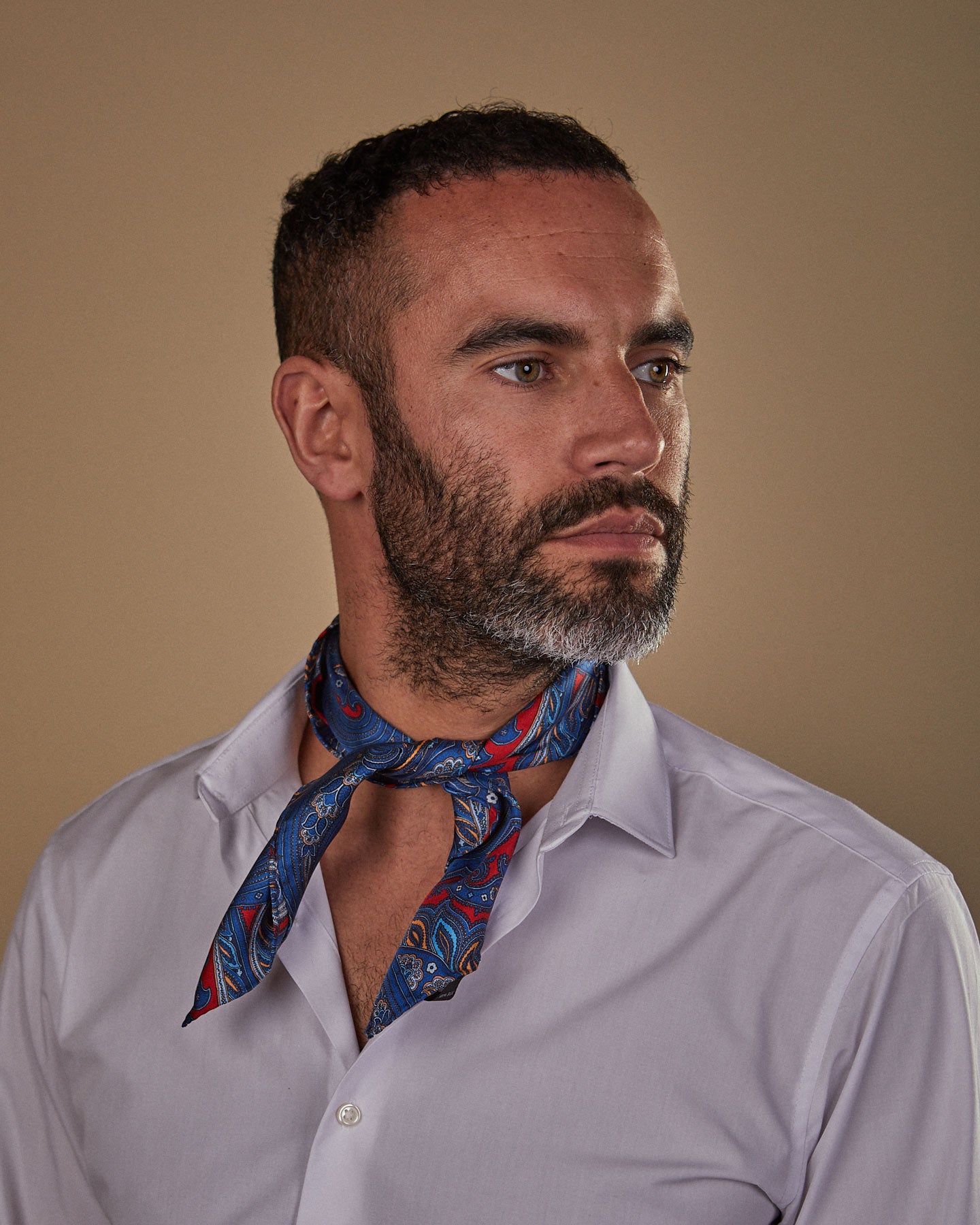 Portrait view of model slightly angled looking to his left, wearing 'The Oxford' red and blue paisley neckerchief tied in a simple front-facing knot.
