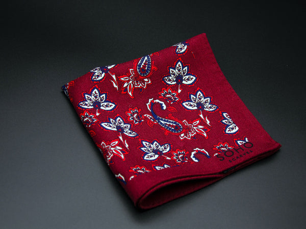 Wool 'Kovalam' pocket square folded showing simple paisley 'tears' and decorative floral patterns on a bright red ground. SOHO Scarves branding clearly visible on bottom-right