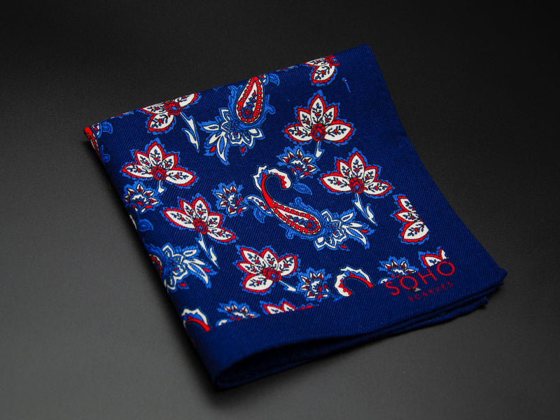 Wool 'Kumarakum' pocket square folded showing simple paisley 'tears' and decorative floral patterns on a deep blue ground. SOHO Scarves branding clearly visible on bottom-right.