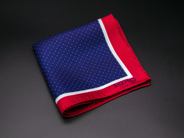 Pure silk 'Ifrane' pocket square folded showing dark blue central square adorned with tiny white dot repeats and framed with a smaller white and a thicker red border. SOHO Scarves branding clearly visible on bottom-right.